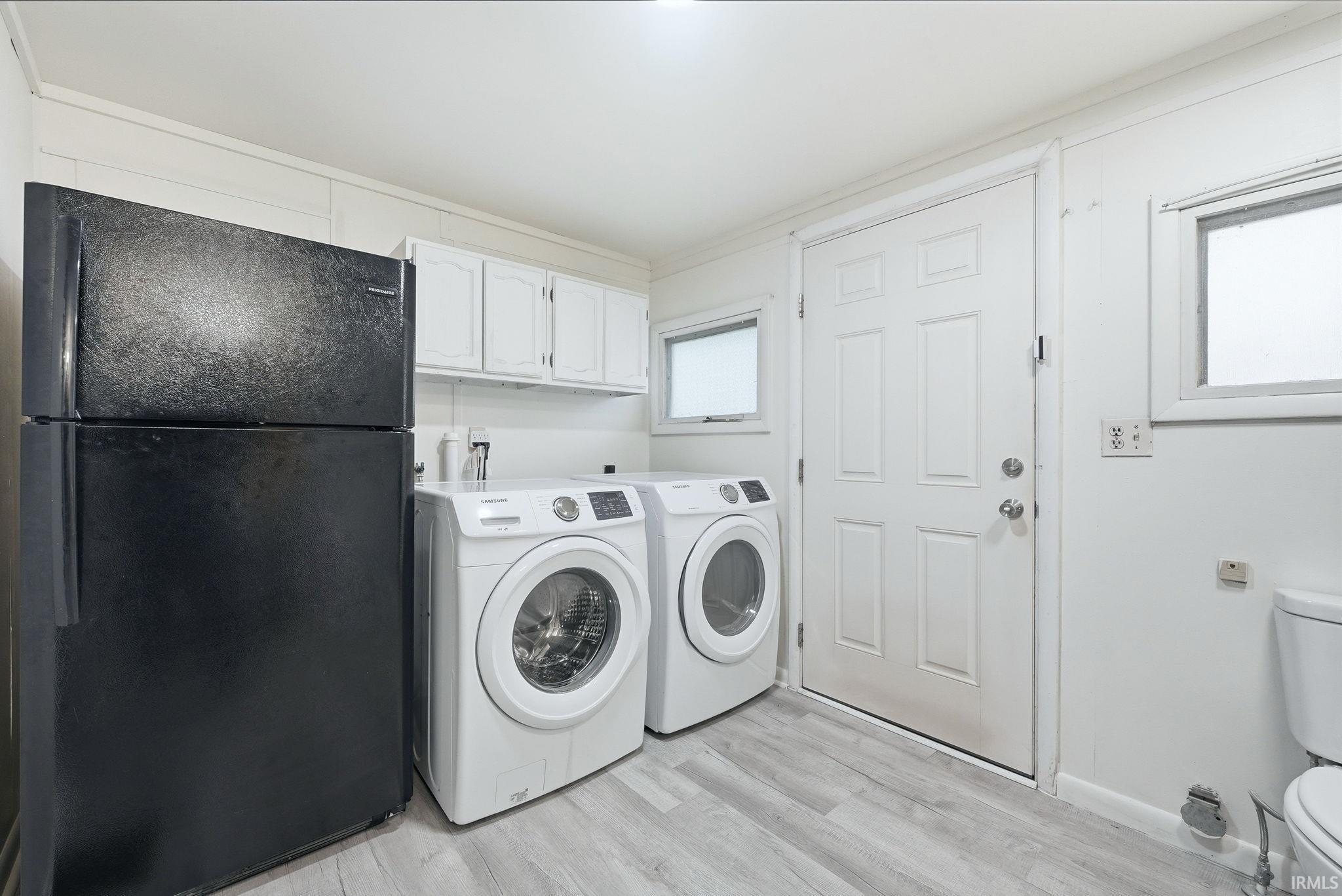 Laundry area with wood-finish flooring, white paneled door, and upper cabinetry