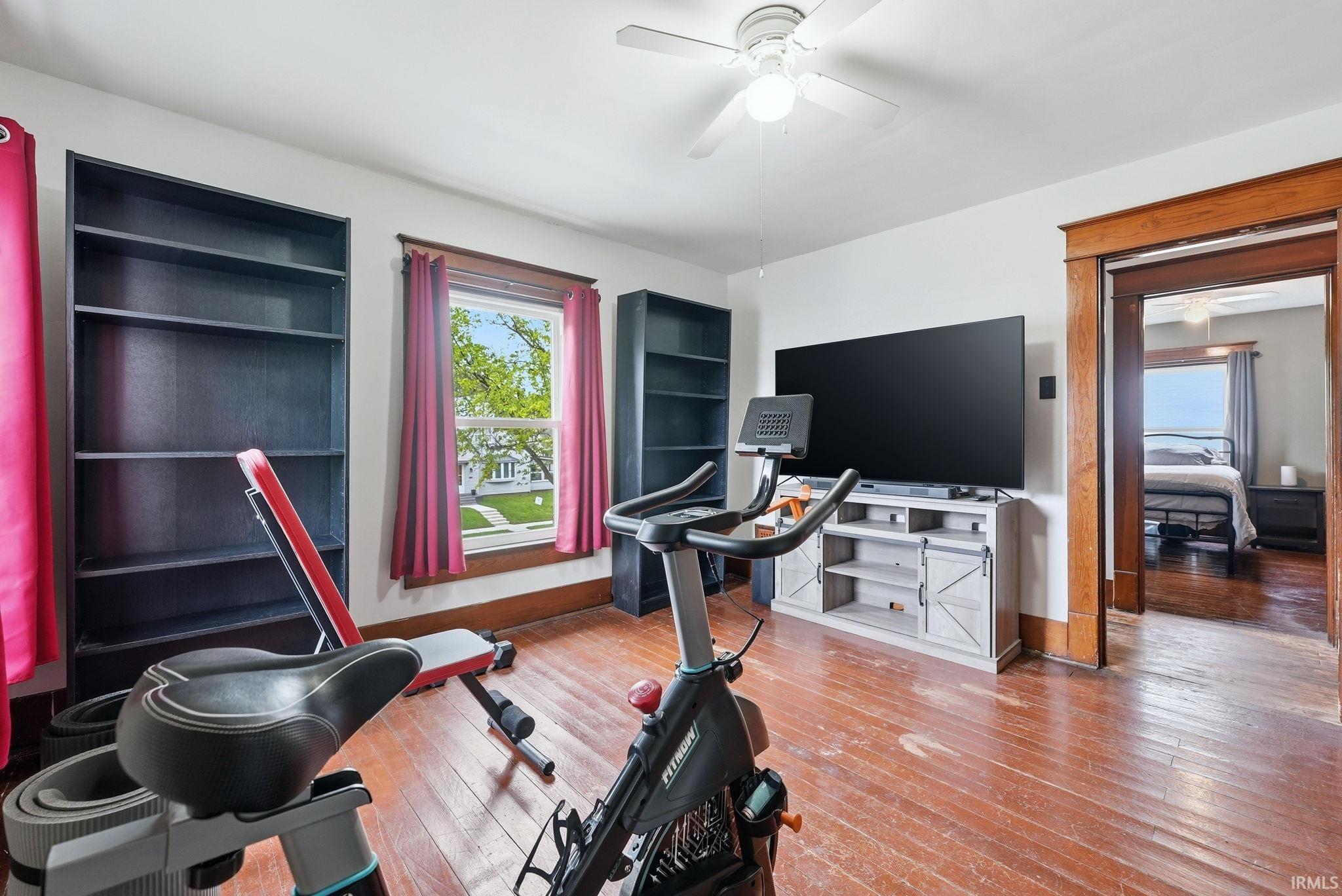 Room featuring wood-finish flooring, a ceiling fan, and substantial wood trim around the window and doorway