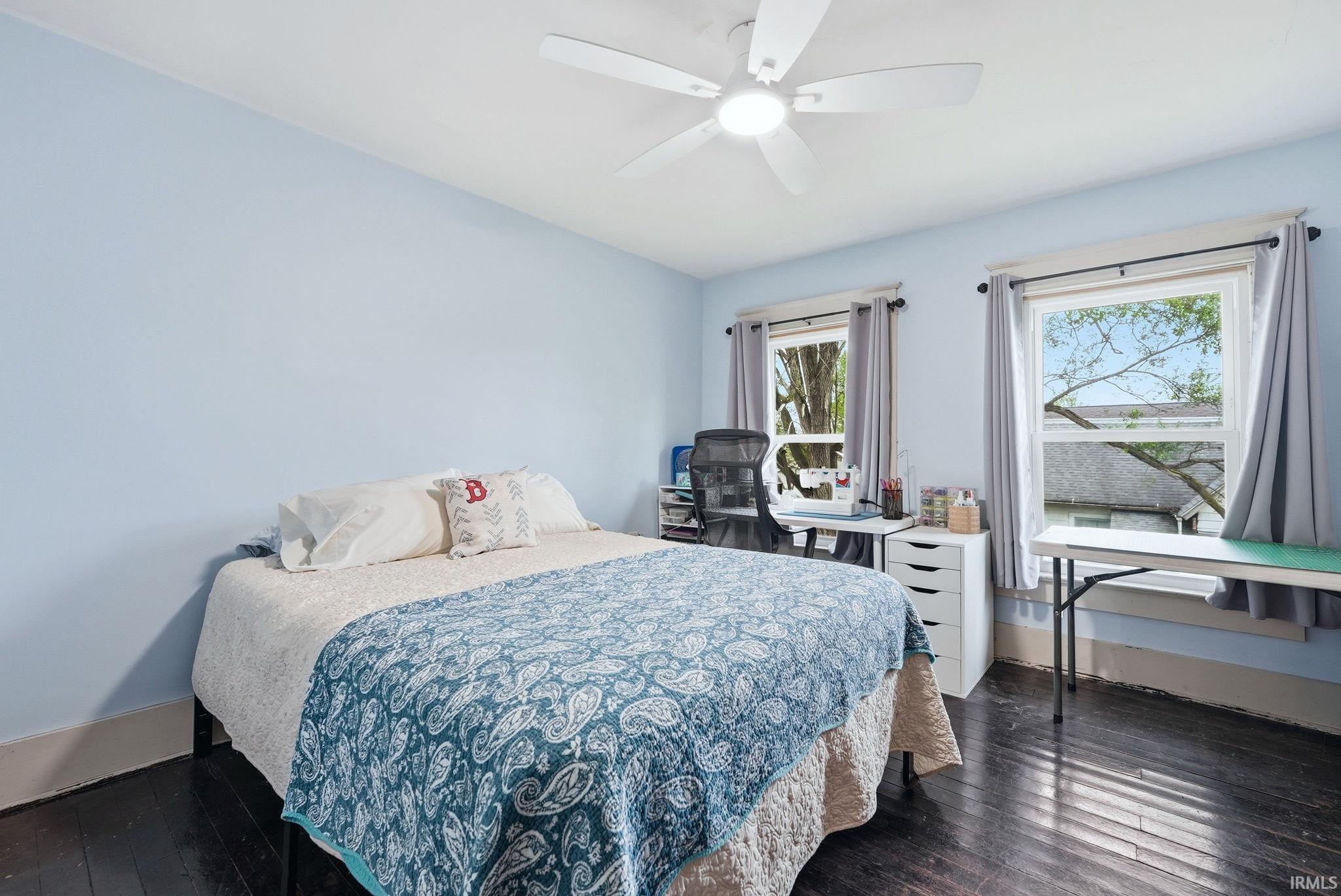 Bedroom featuring light blue walls, dark wood-finish flooring, and a white ceiling fan