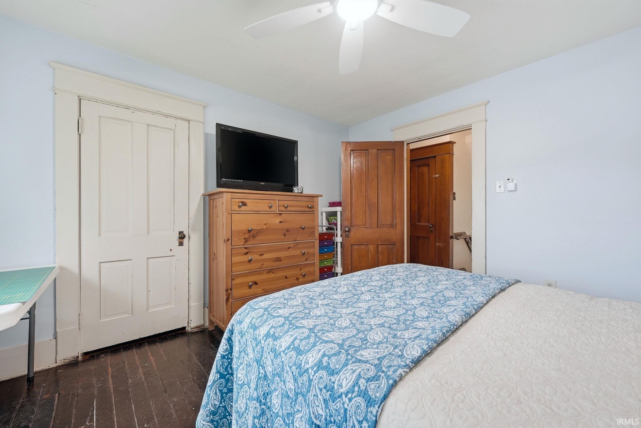 Interior room featuring dark wood-finish flooring, light blue wall paint, a white ceiling fan, and white trim around doorways