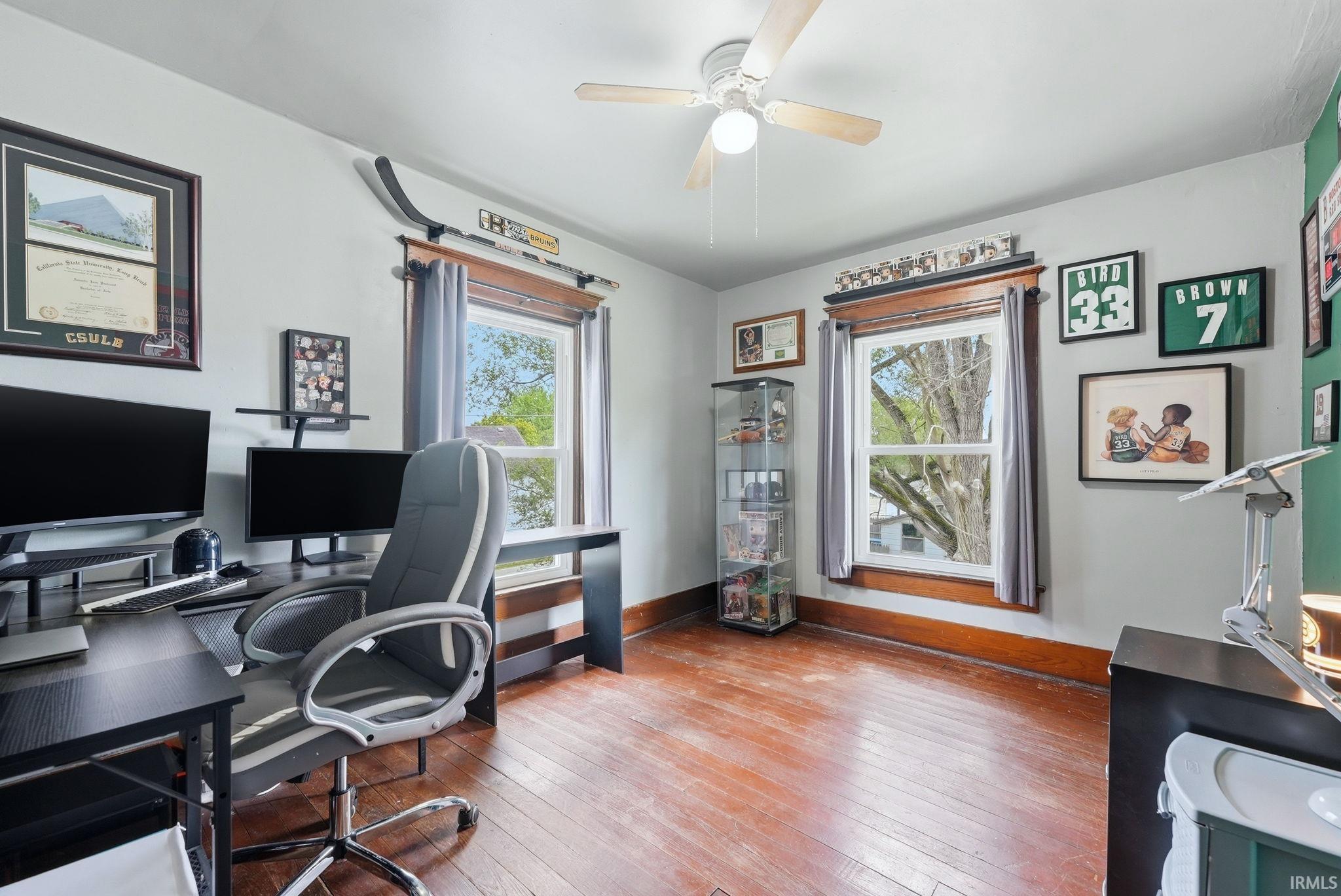 Hardwood-finish flooring featuring a ceiling fan, dual windows with wood trim, and a built-in glass display cabinet