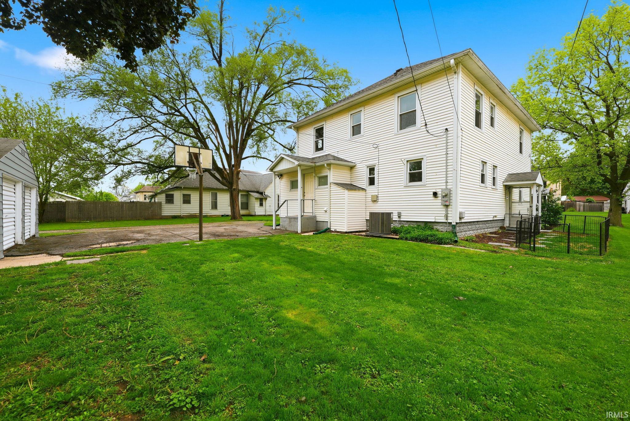 Expansive grassy yard with a two-story white siding residence featuring multiple windows, a rear entrance with a small porch, and a detached two-car garage