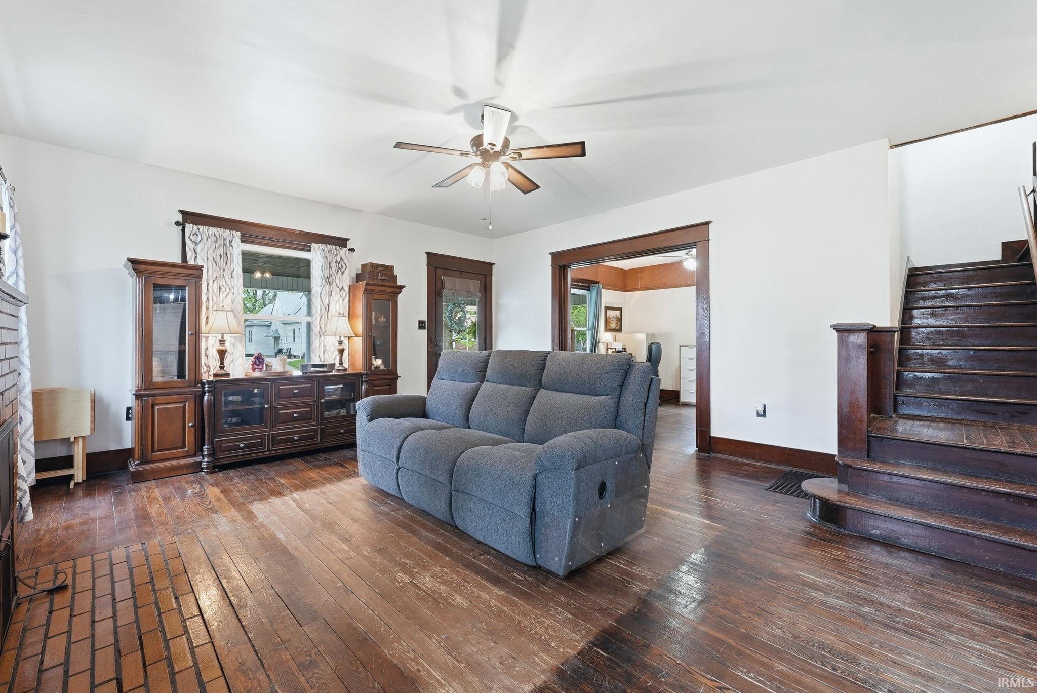 Spacious room featuring wood-finish flooring, a ceiling fan, and prominent wood trim details around windows and doorways