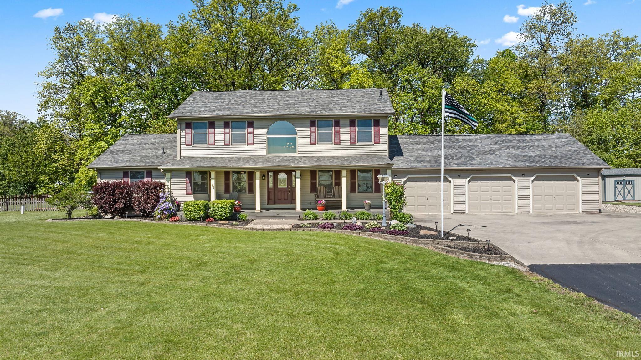 Two-story residence featuring a covered front porch, an arched transom window, a three-car garage, an expansive paved driveway, and mature landscaping