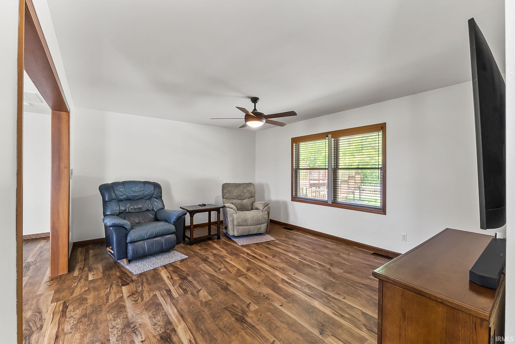 Spacious living area featuring wood-finish flooring, a ceiling fan, and white walls