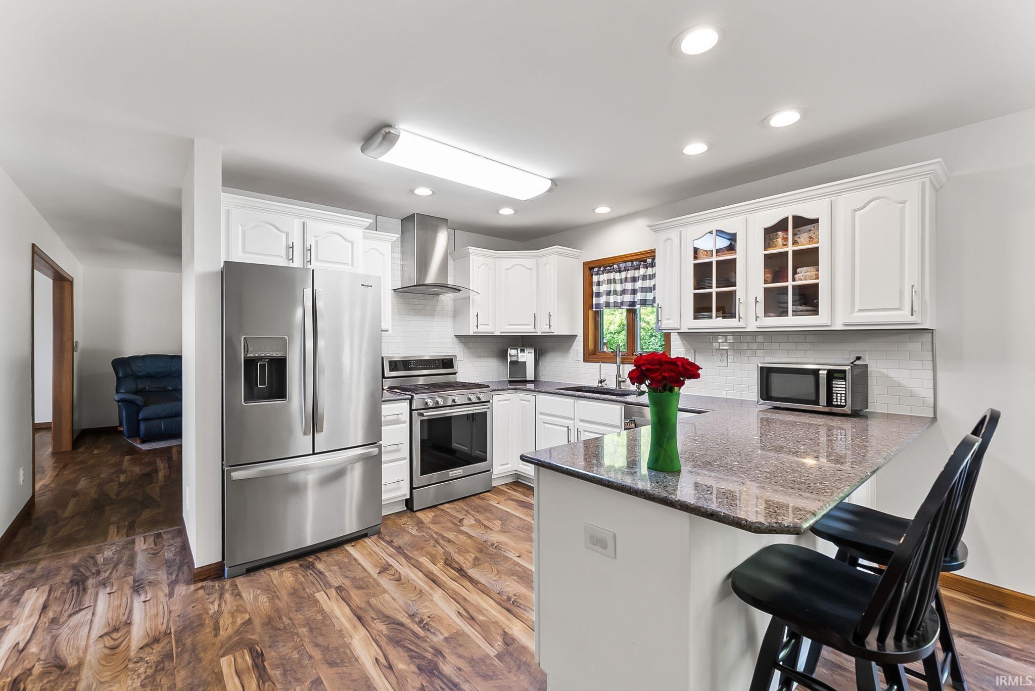 Kitchen featuring white cabinetry, stainless steel appliances, a tile backsplash, and wood-finish flooring