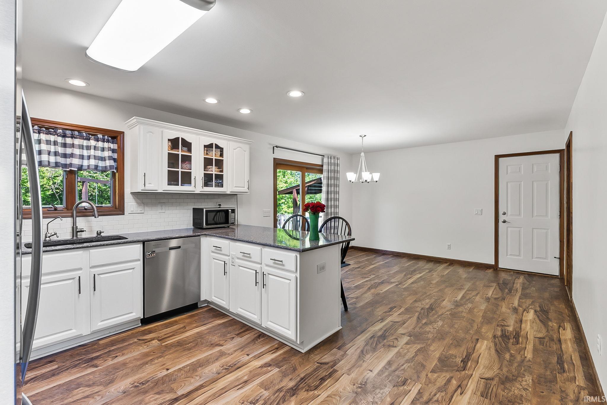 Kitchen featuring white shaker cabinetry, stainless steel dishwasher, a center island with countertop seating, and wood-finish flooring