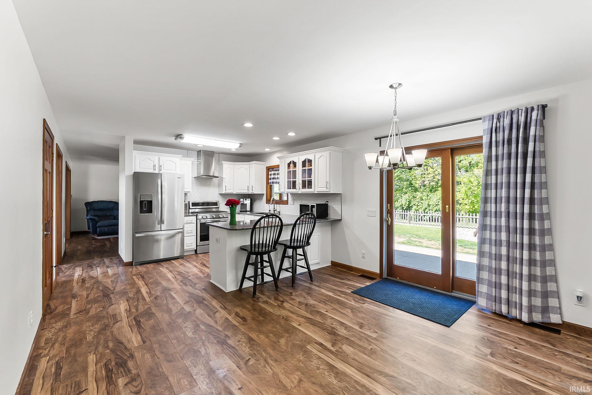 Kitchen featuring white cabinetry, stainless steel appliances, a central island with countertop seating, wood-finish flooring, and sliding glass doors