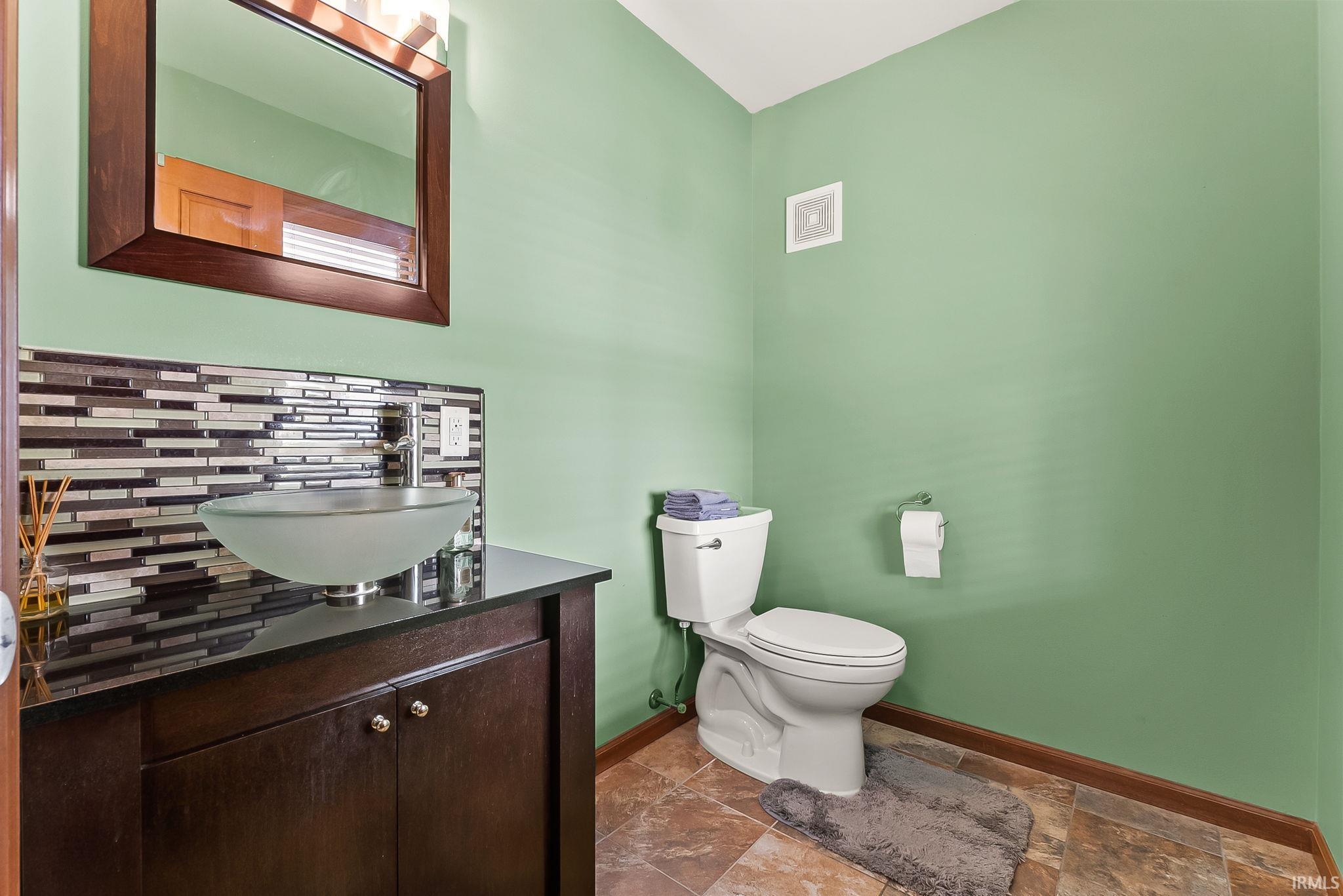 Bathroom featuring a vessel sink, dark wood-finish vanity with storage, mosaic tile backsplash, and a contemporary mirror