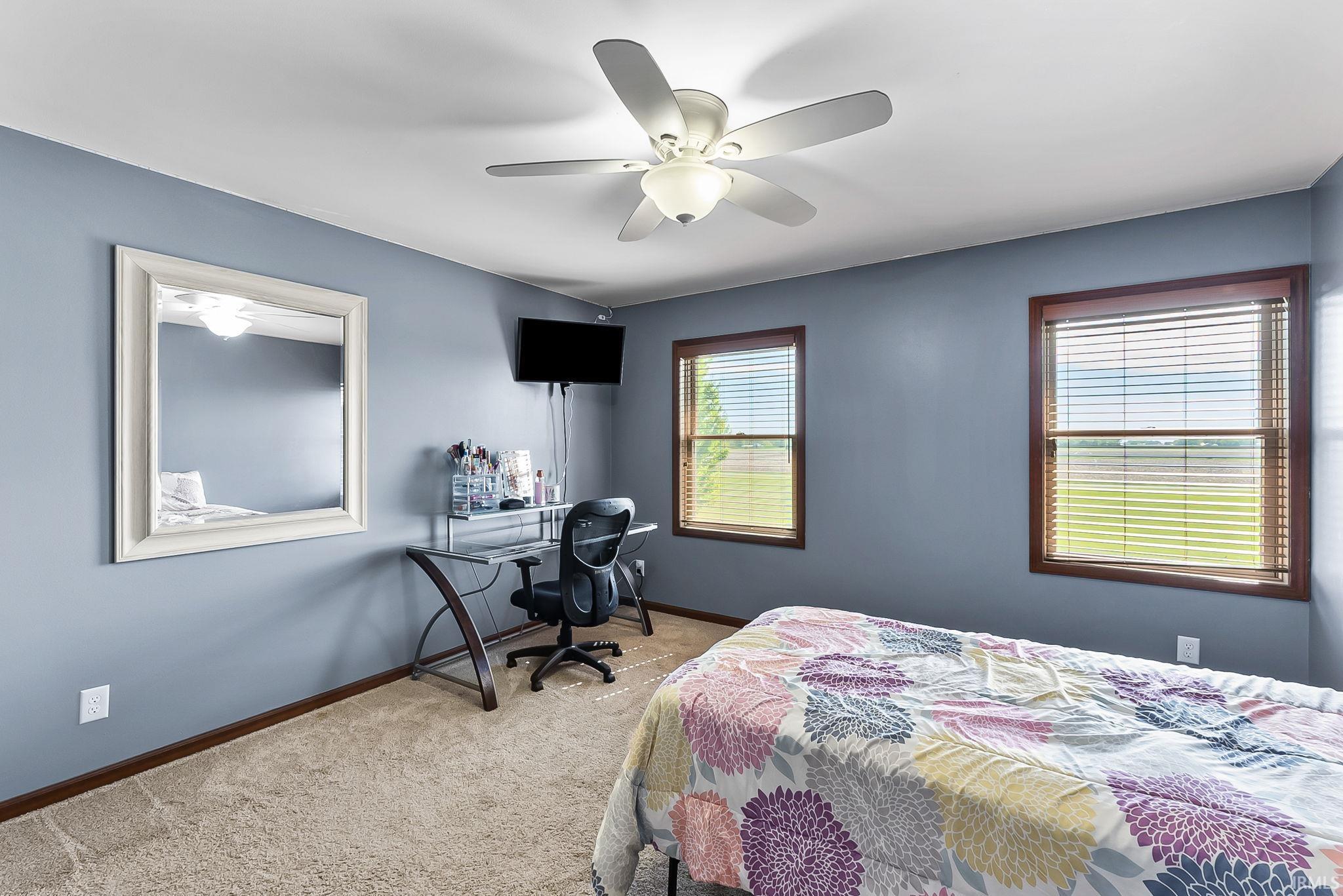 Carpeted room featuring two windows with wood-finish trim and integrated blinds, a ceiling fan with light fixture, and a neutral color palette