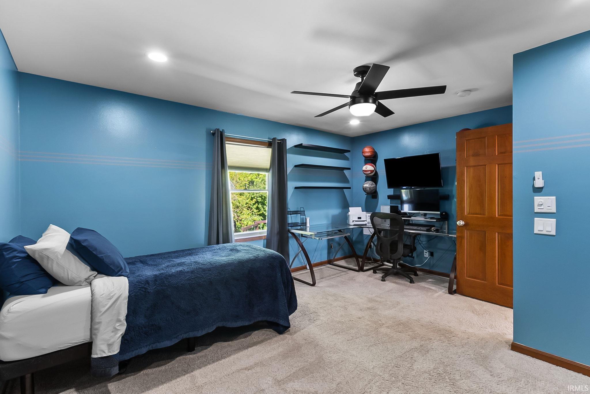 Spacious room featuring neutral carpeting, a window with natural light, a ceiling fan with integrated lighting, recessed overhead lighting, and built-in wall shelving