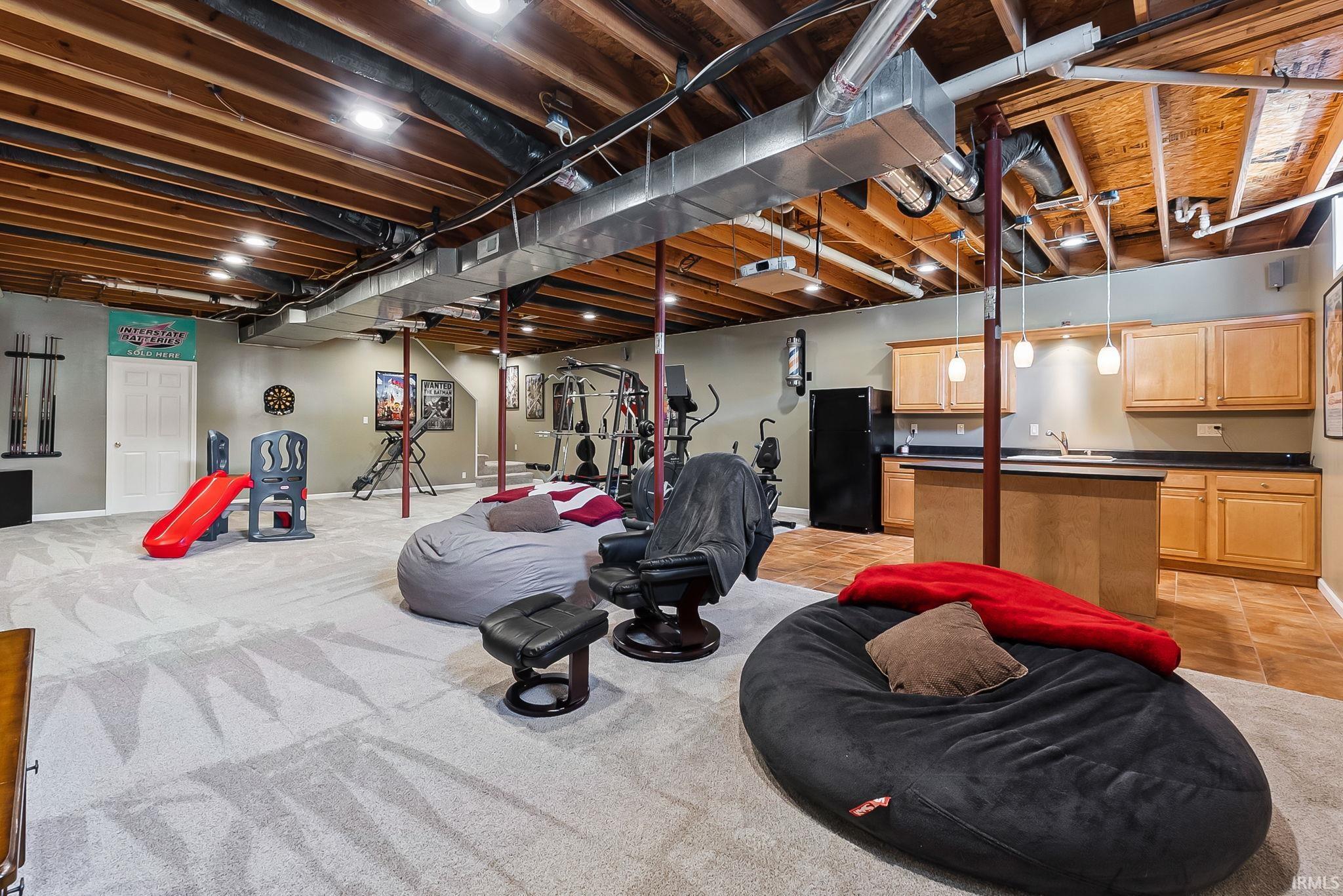 Expansive lower level featuring recessed lighting, exposed ceiling joists, and a wet bar with pendant lighting