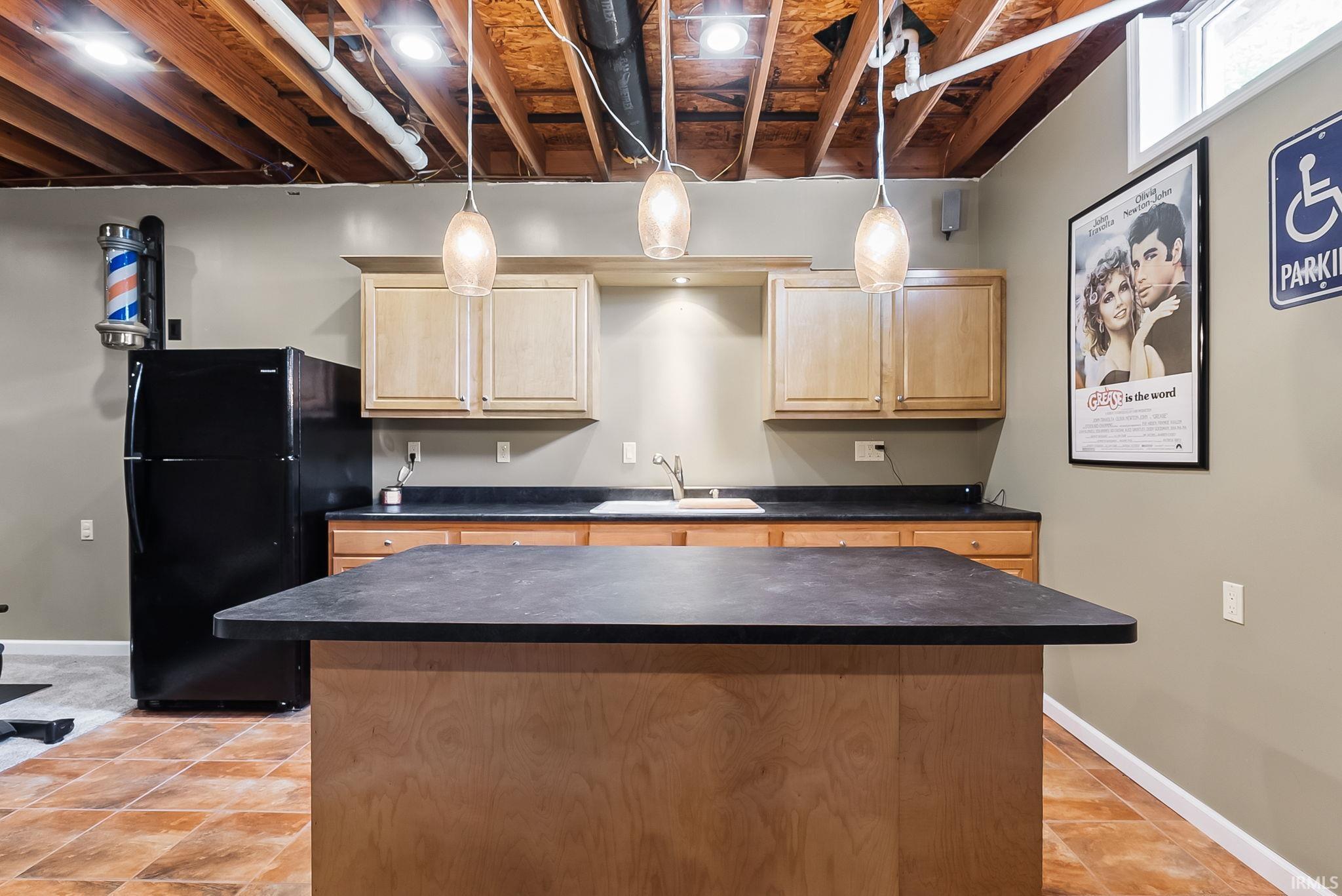 Kitchenette featuring a central island with a dark countertop, light wood cabinetry, and a stainless steel sink