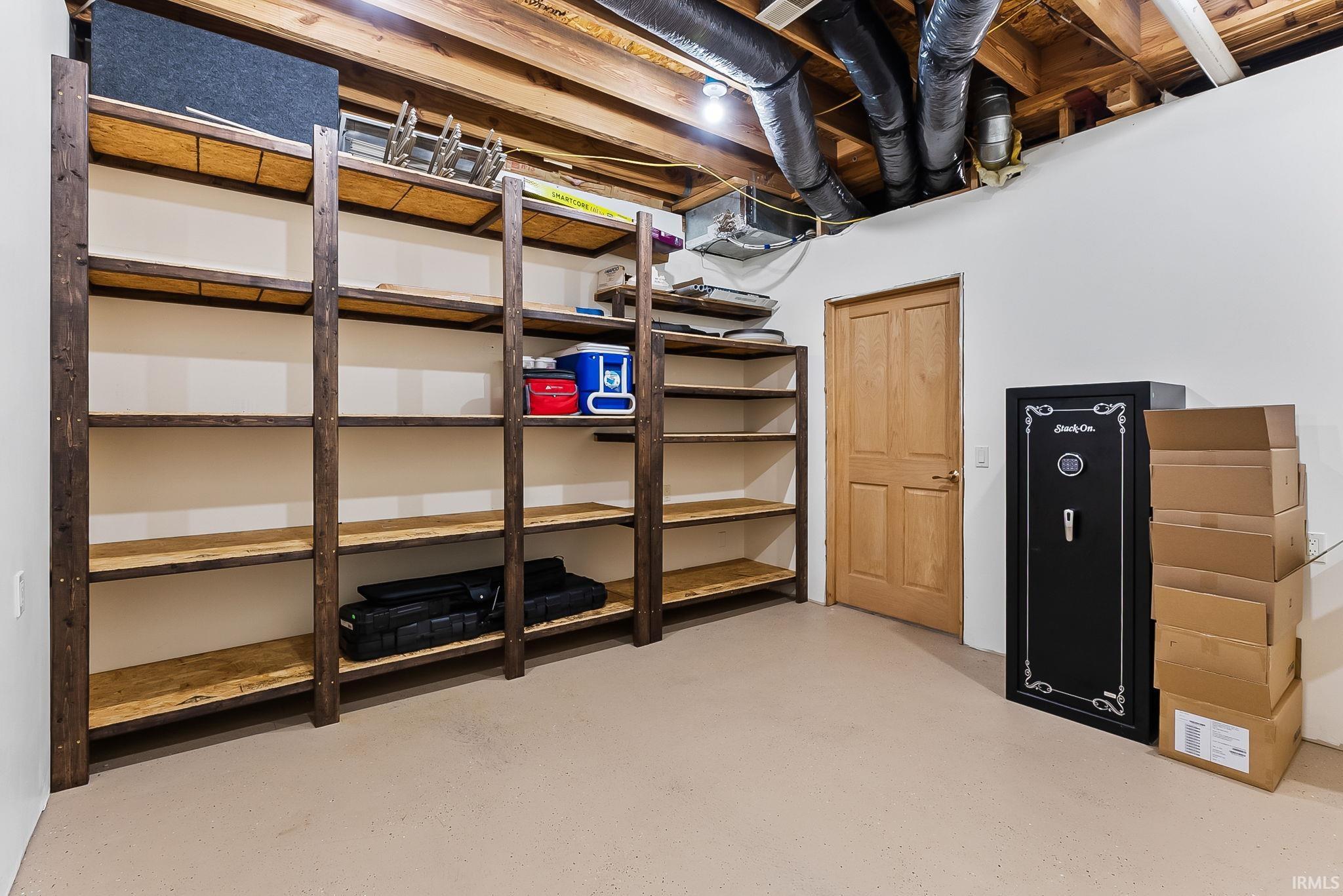 Spacious utility area featuring extensive built-in shelving, durable flooring, a natural wood paneled door, and exposed ceiling joists with ductwork