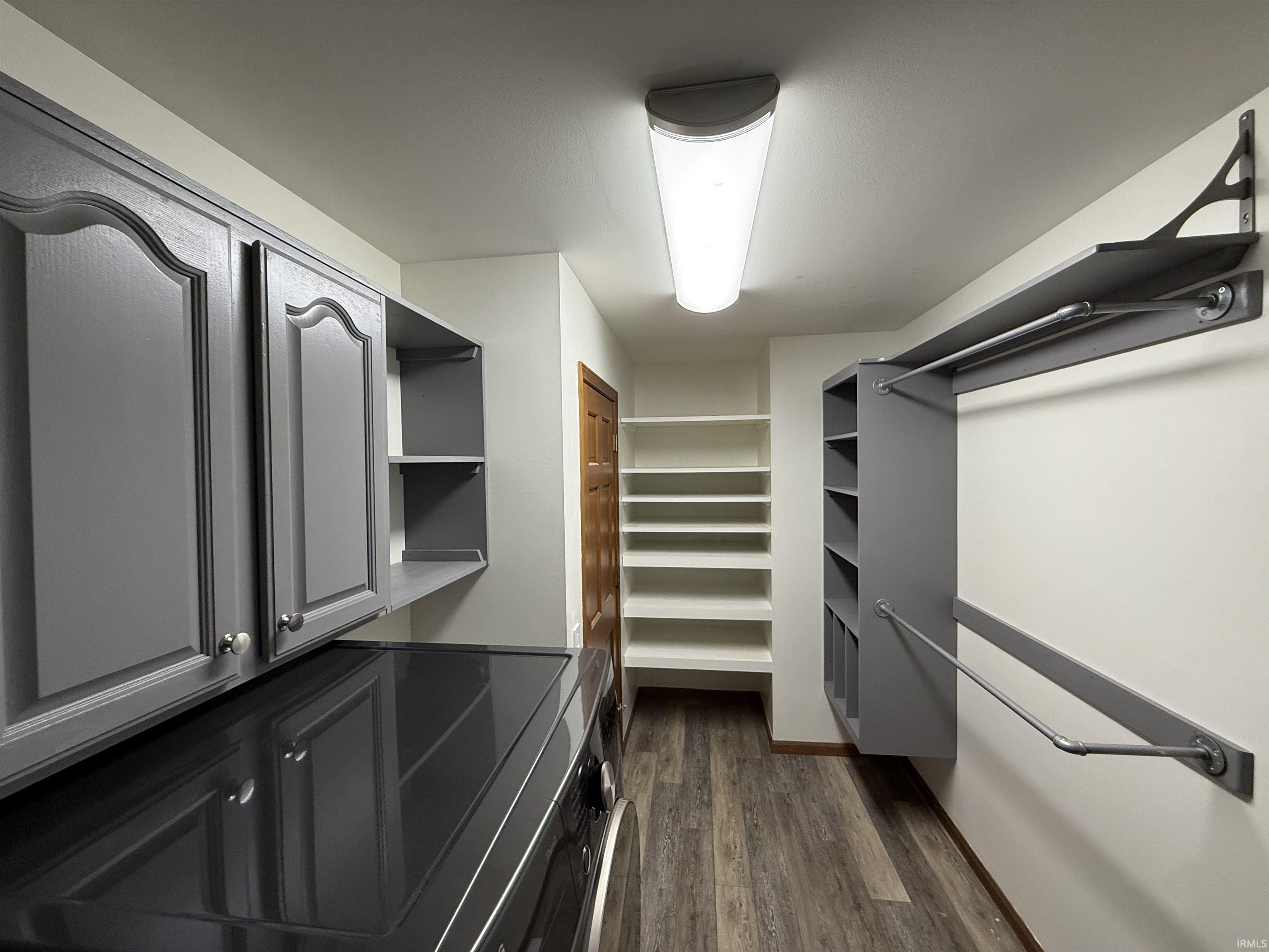 Laundry area featuring overhead cabinetry, extensive built-in shelving, hanging rods, wood-finish flooring, and a flush-mount ceiling light fixture