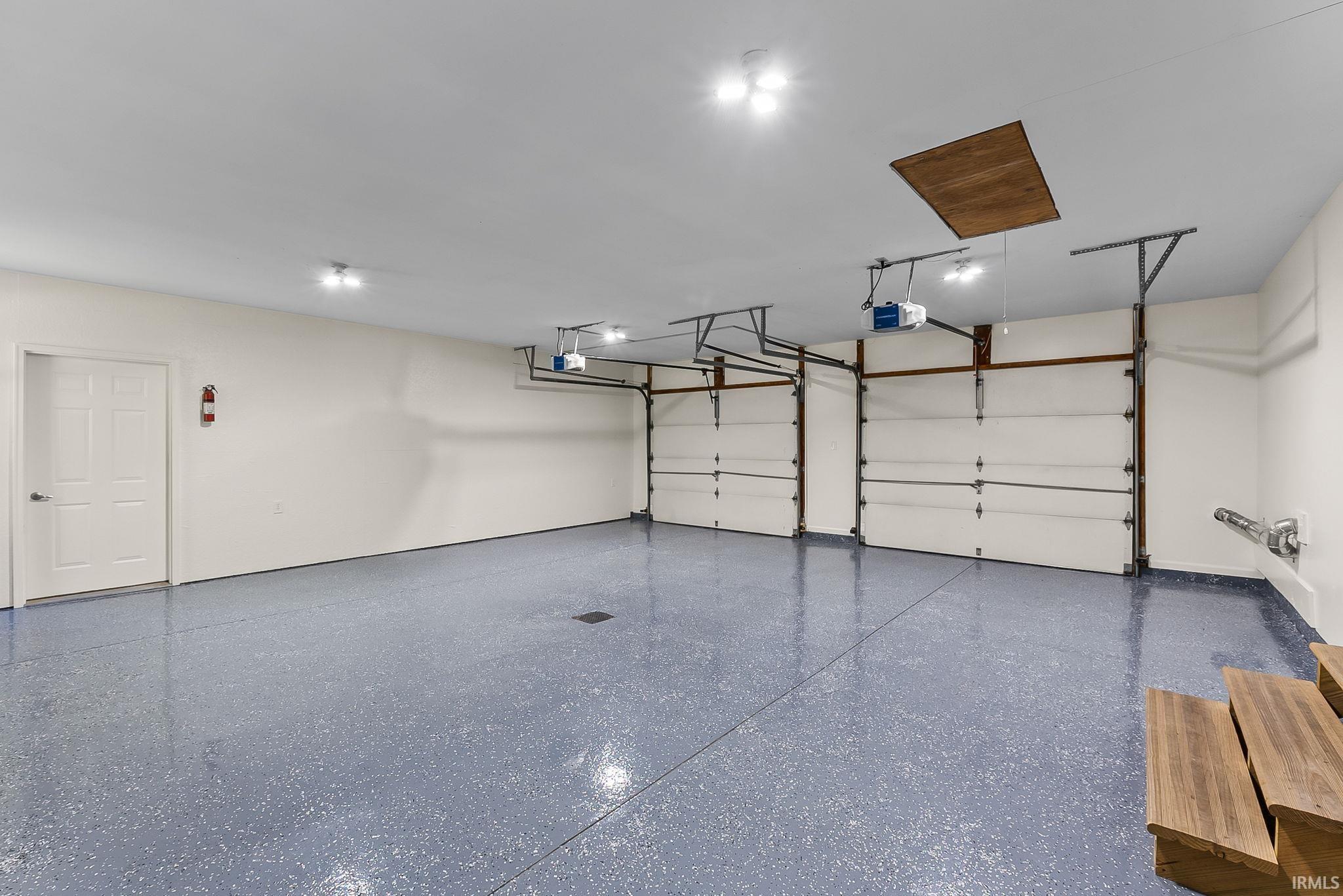 Spacious garage featuring two overhead doors, a speckled epoxy floor, white walls, and recessed lighting