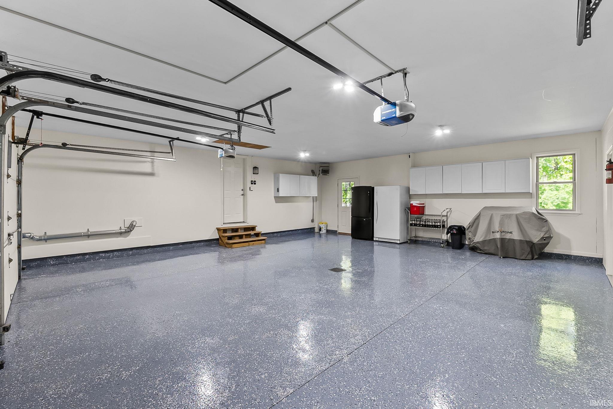 Spacious garage featuring a speckled epoxy floor, white walls, multiple windows, and extensive white cabinetry
