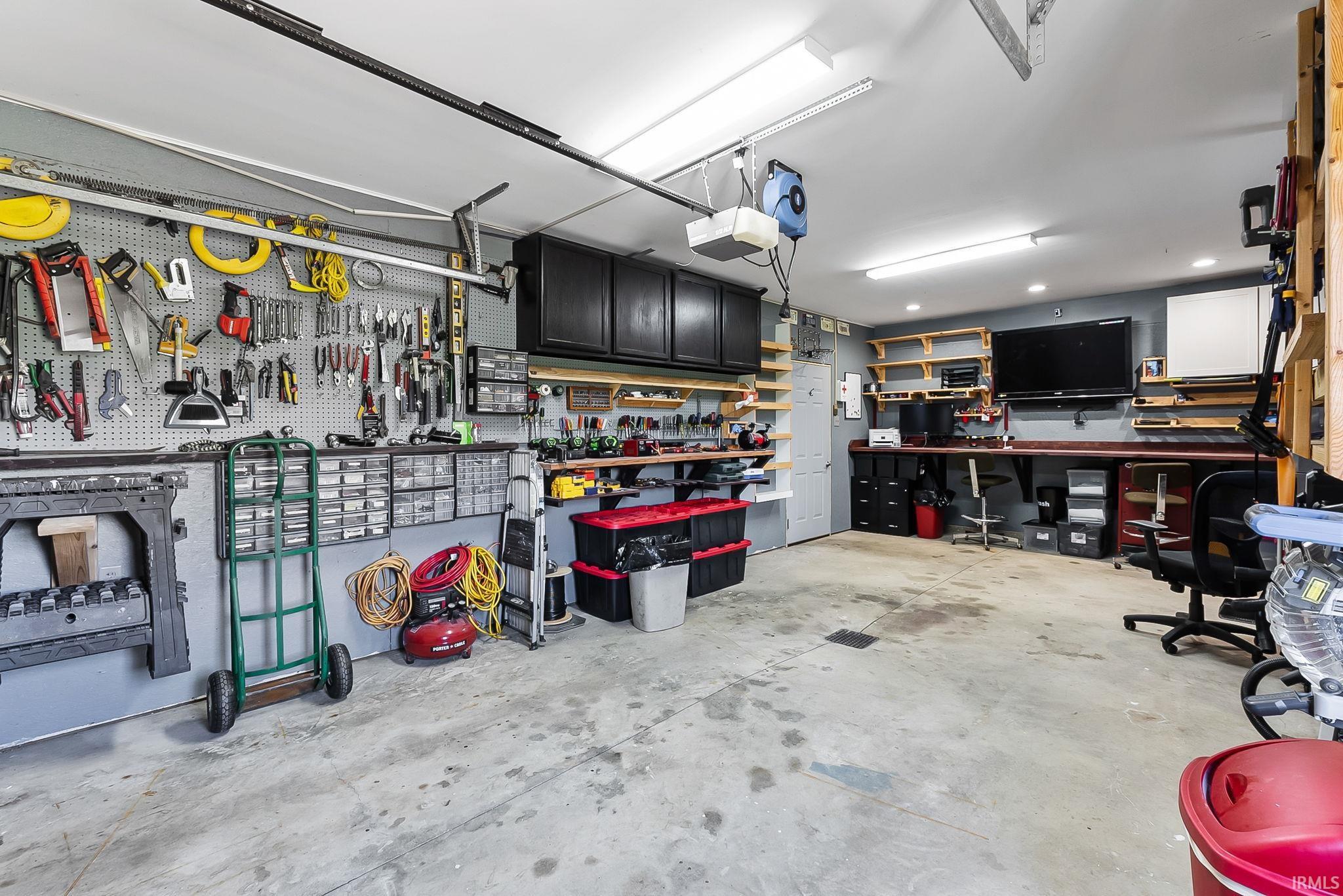 Spacious garage featuring concrete flooring, extensive pegboard organization, built-in shelving, a dedicated workbench area, and overhead lighting