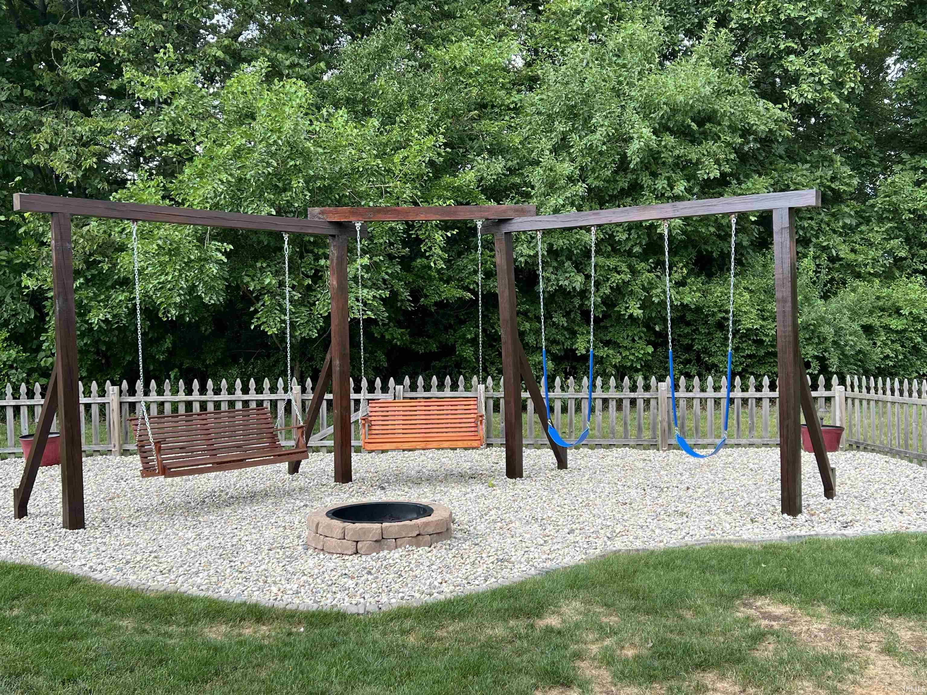 Outdoor play structure featuring multiple swings, a built-in fire pit with brick surround, and a gravel base
