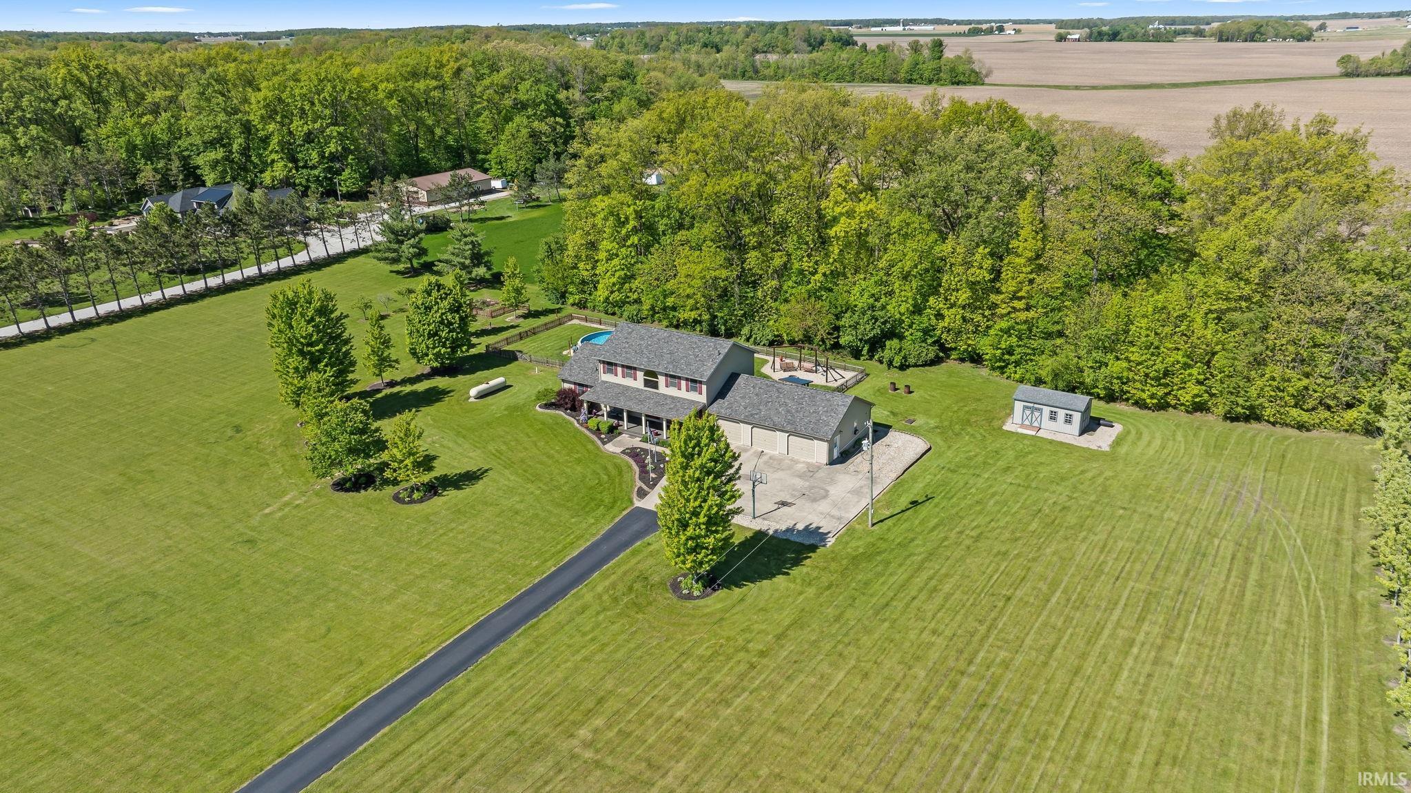 Expansive property featuring a two-story residence with a covered front porch, an attached garage, a paved driveway, and a visible swimming pool