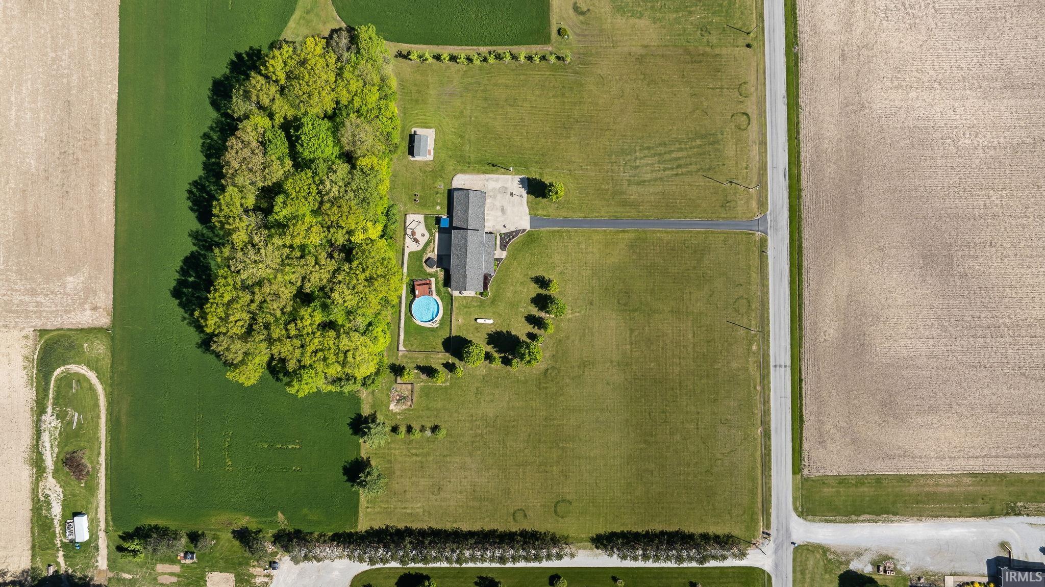 Expansive property featuring a central residence, large detached outbuilding, a circular above-ground pool, and mature tree clusters