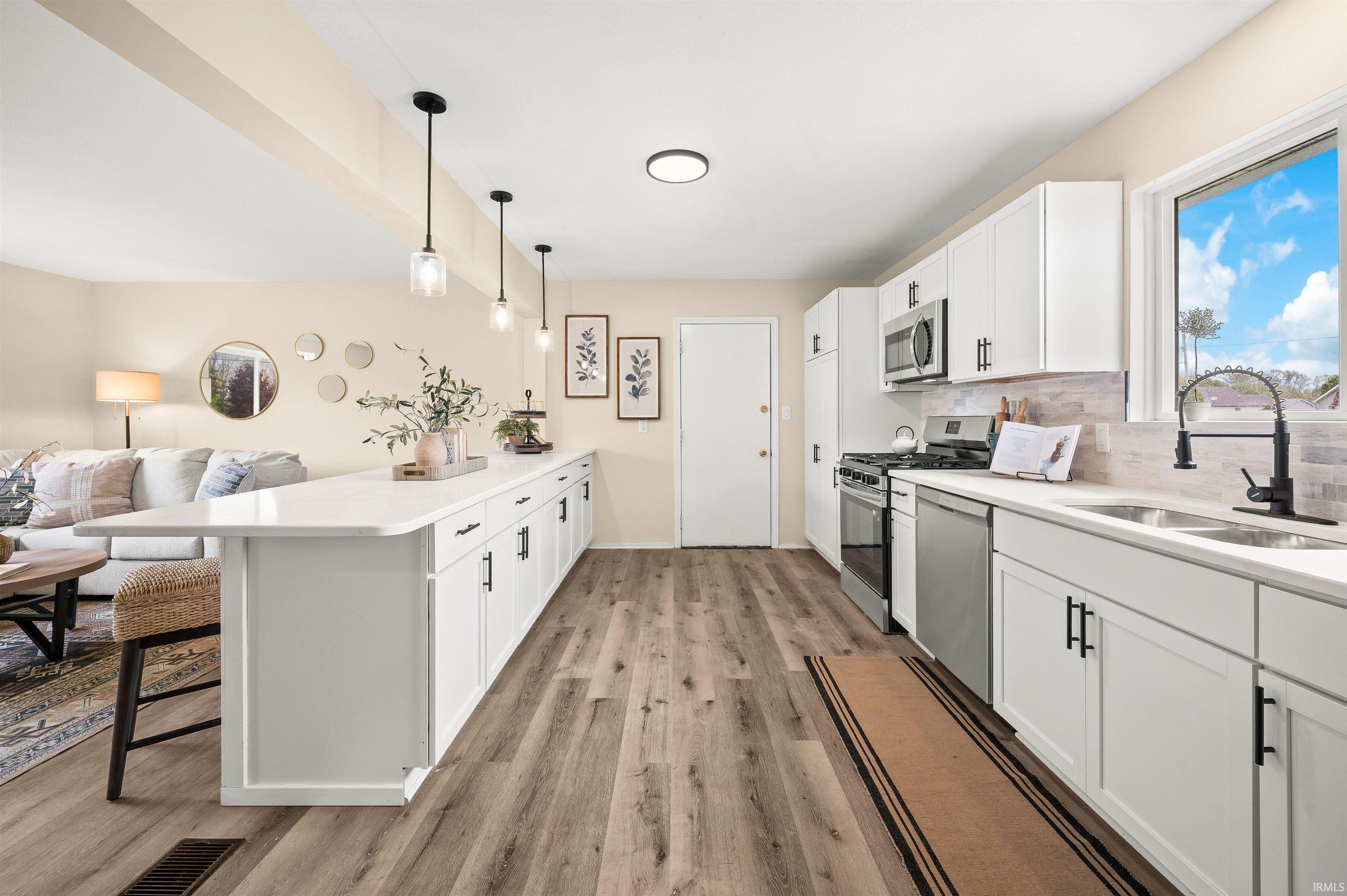 Kitchen featuring an expansive island with a quartz countertop, white cabinetry, wood-finish flooring, stainless steel appliances, and pendant lighting