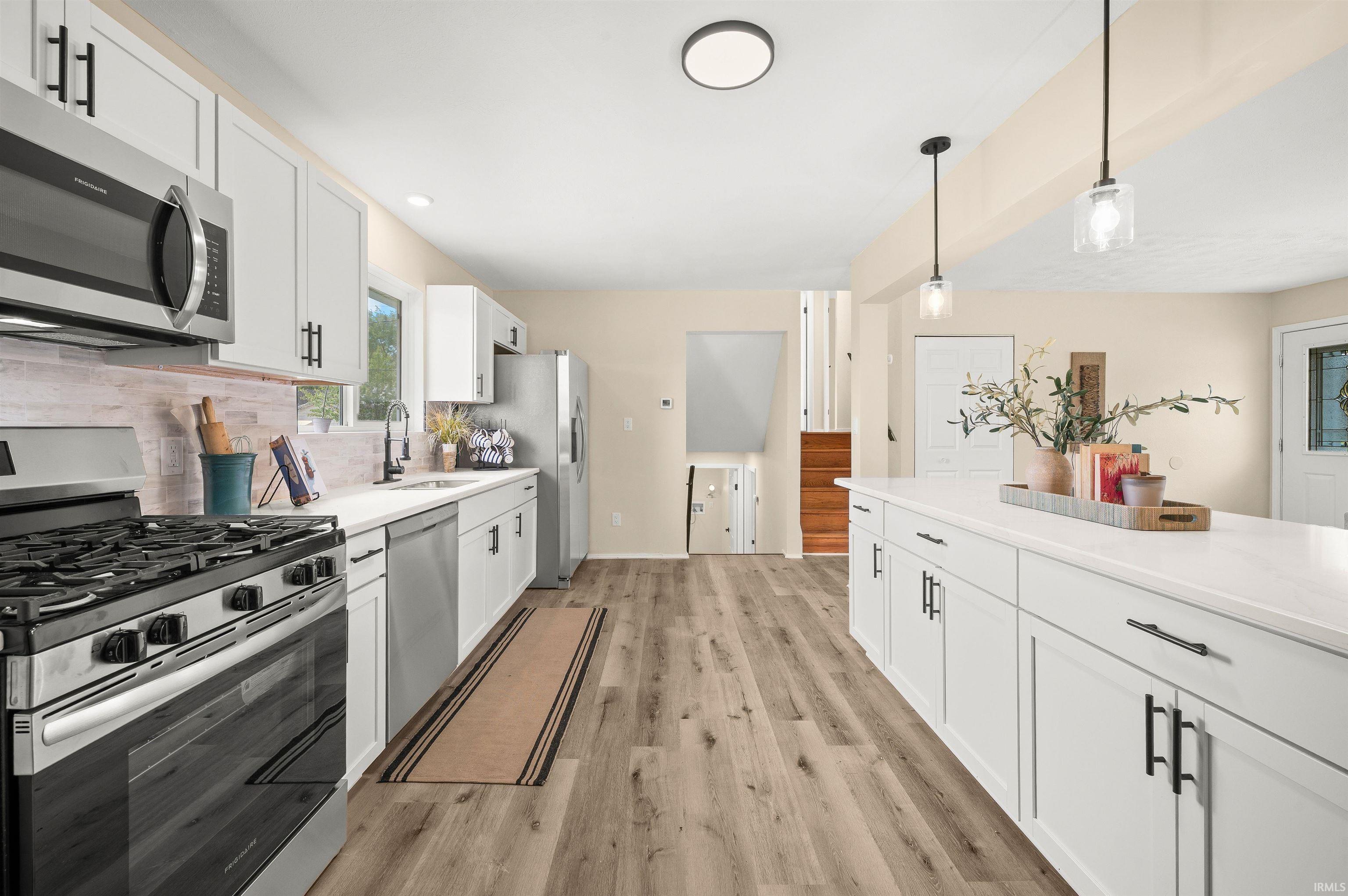 Modern kitchen with an expansive island, white cabinetry, stainless steel appliances, and wood-finish flooring