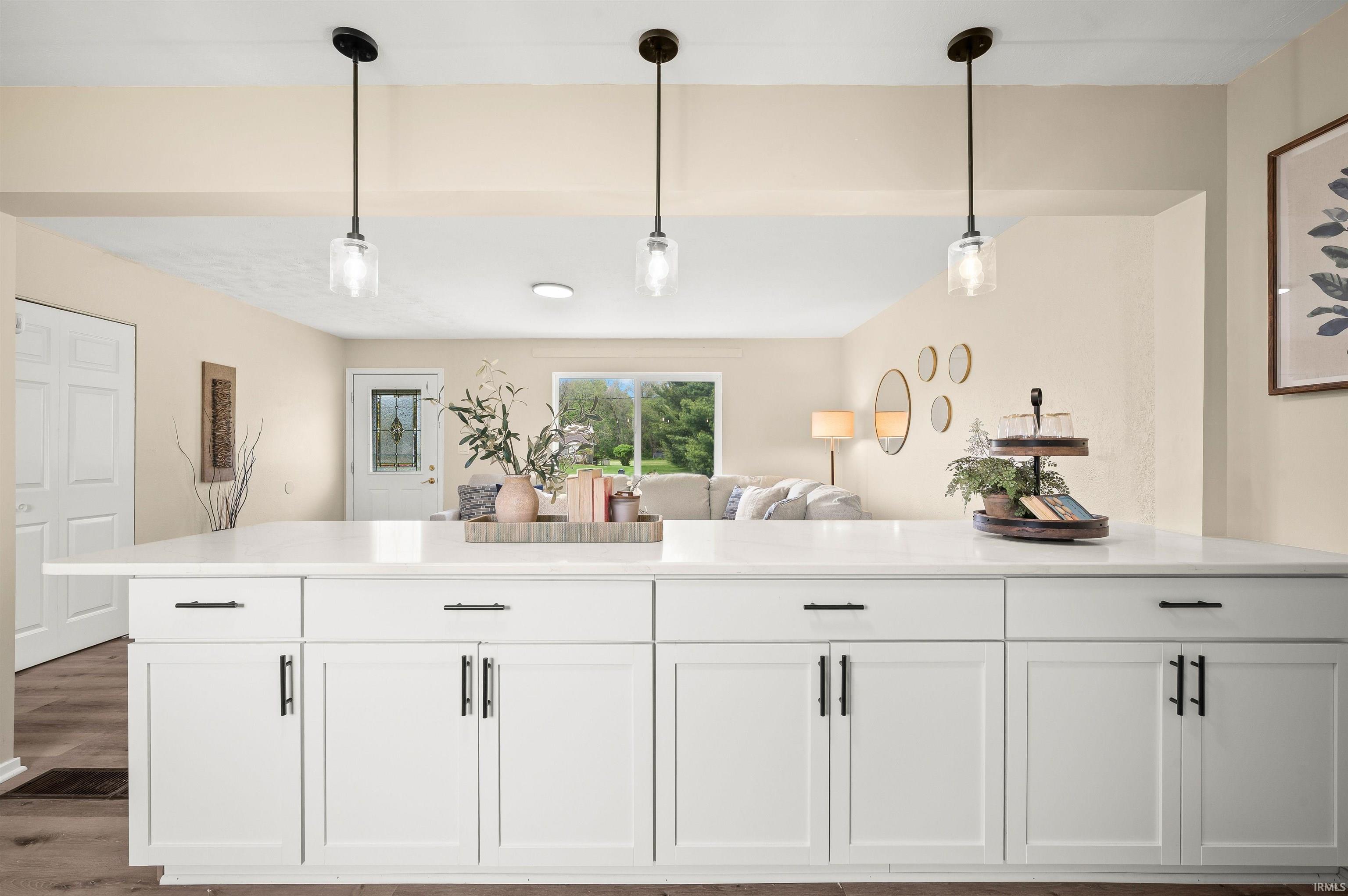 Kitchen island featuring white cabinetry, black hardware, a light-toned countertop, and three pendant lights
