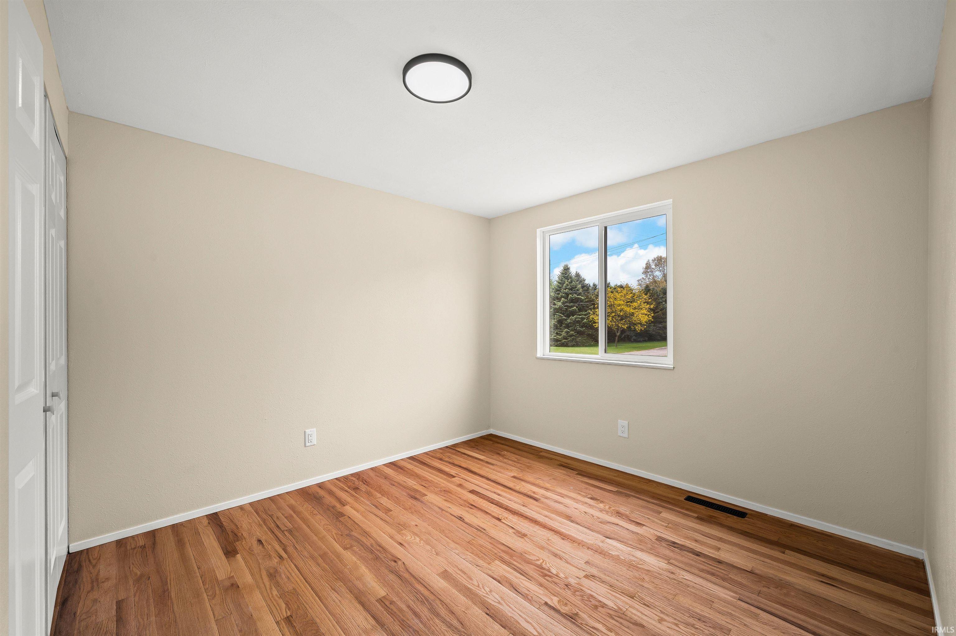 Room featuring wood-finish flooring, neutral wall paint, and a white trim baseboard
