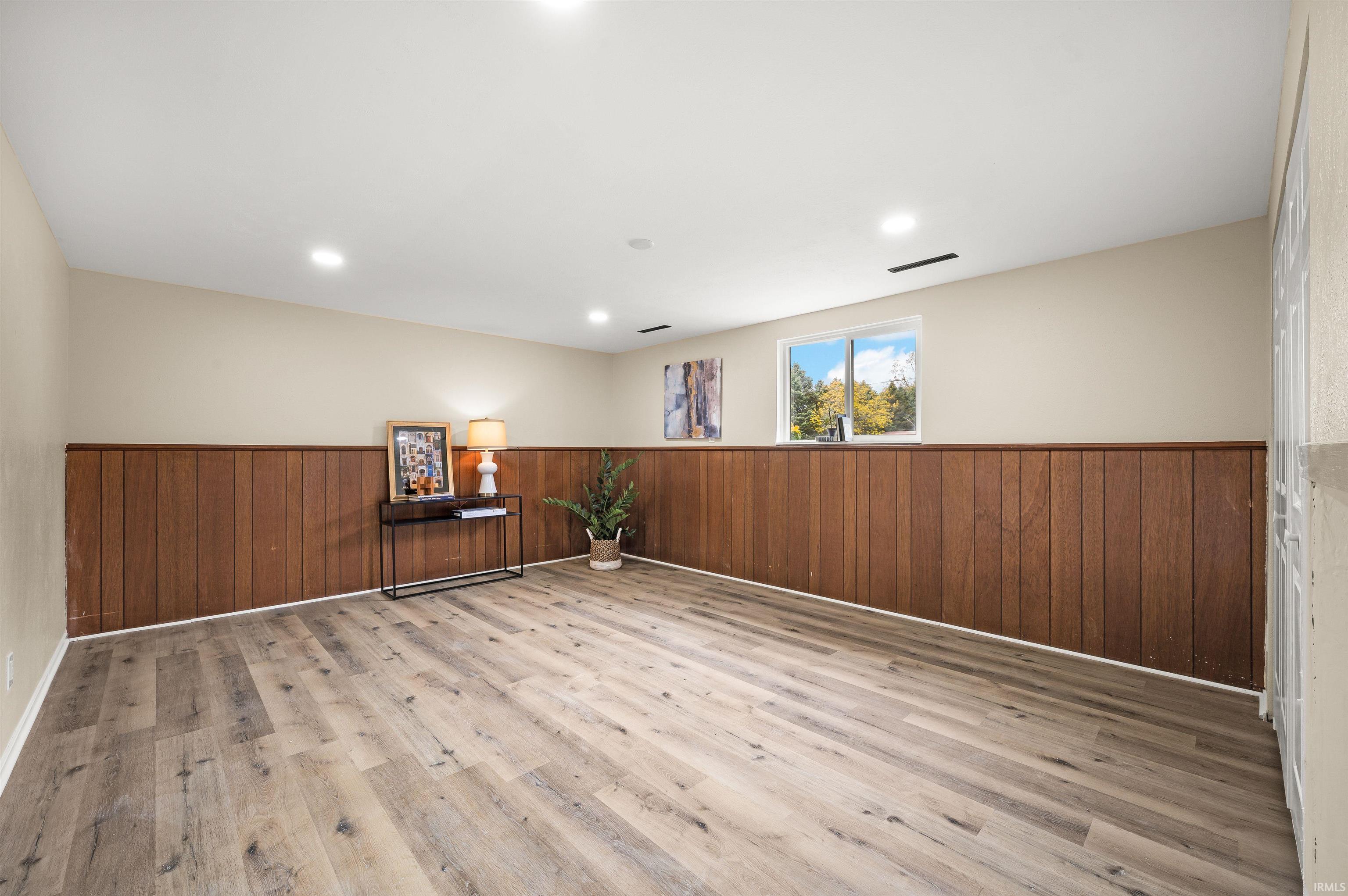 Spacious room featuring wood-finish flooring, wood paneling, recessed lighting, and a single window