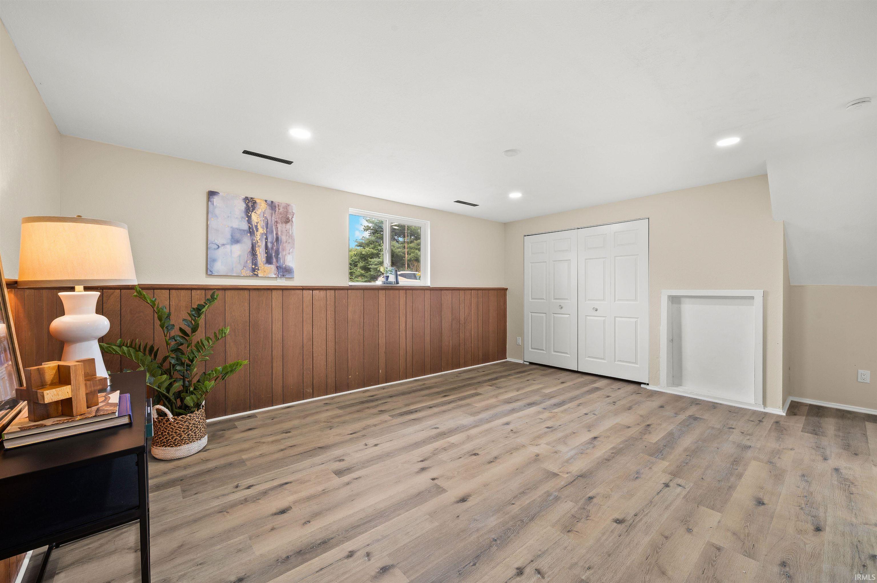 Spacious room featuring wood-finish flooring, half-wall wood paneling, recessed lighting, and a double-door closet