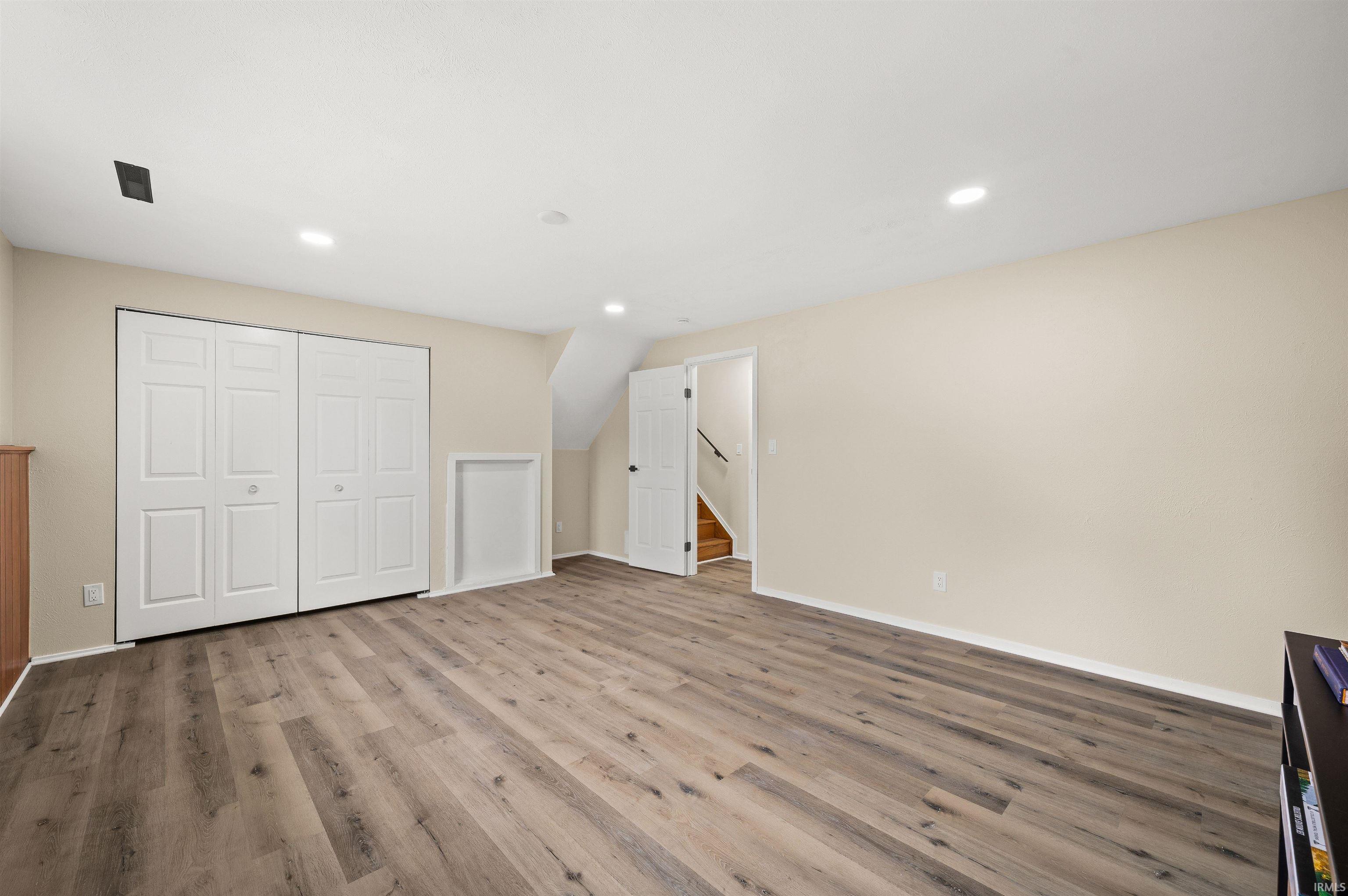 Spacious room featuring wood-finish flooring, neutral-toned walls, recessed lighting, and a bi-fold closet