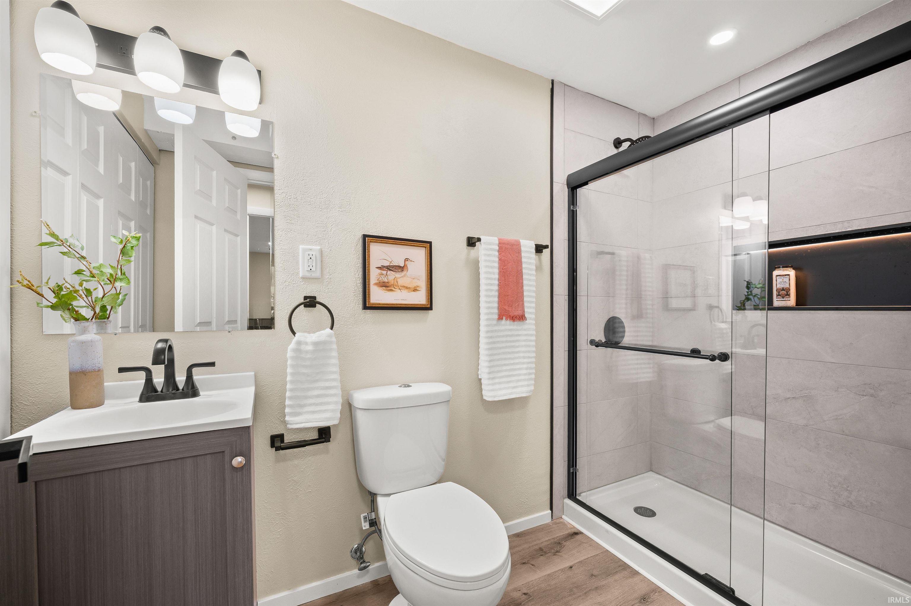 Contemporary bathroom featuring a glass-enclosed shower with a recessed shelf, wood-finish flooring, a vanity with integrated sink, and matte black fixtures