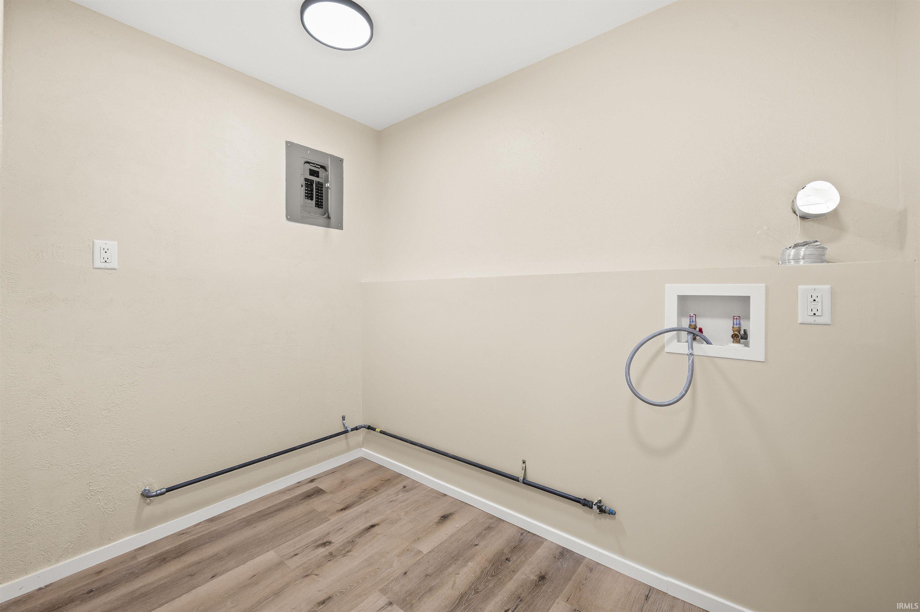 Dedicated utility space featuring light beige wall paint, wood-finish flooring, and white baseboards