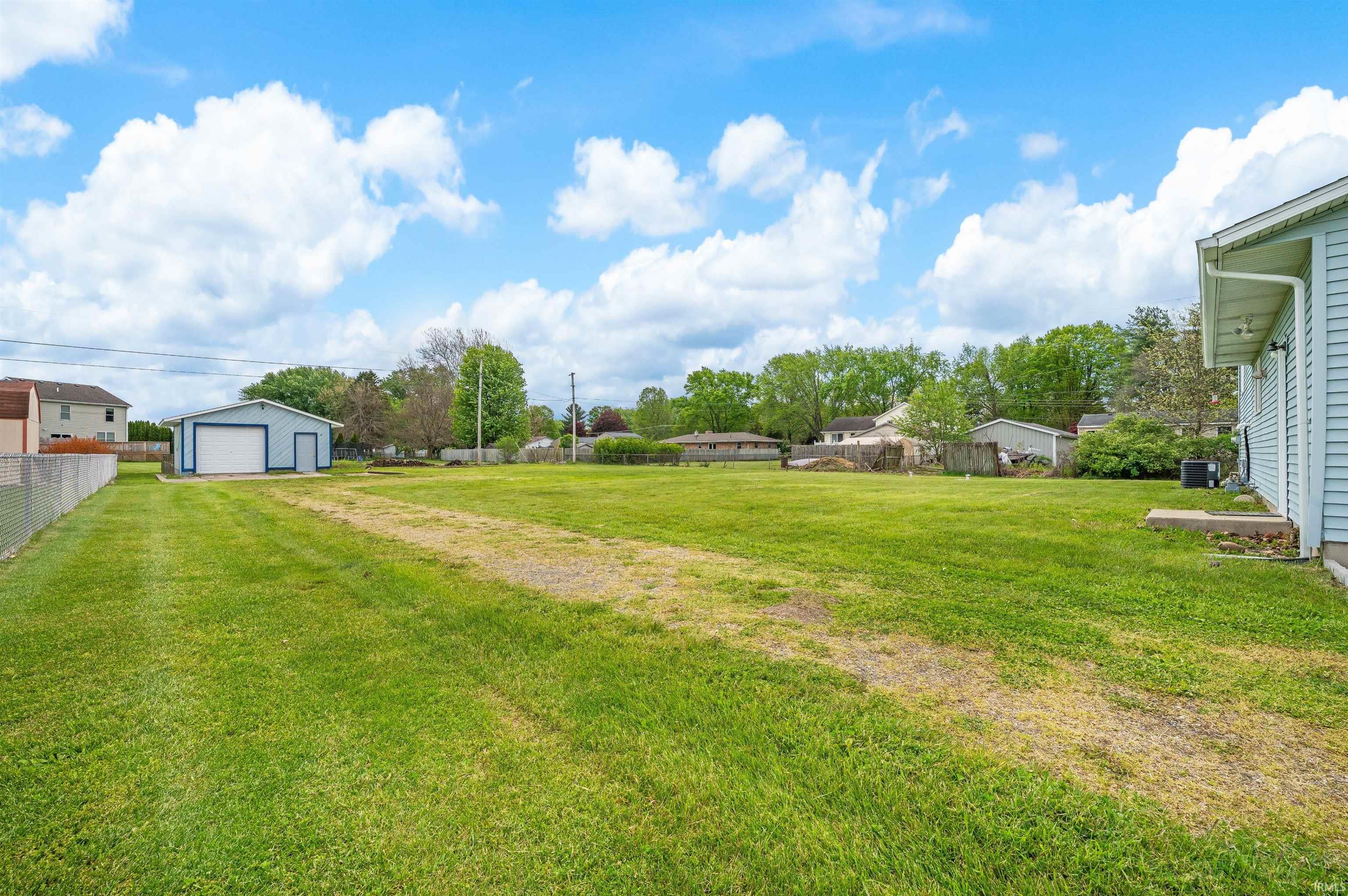 Expansive green lawn with a detached blue outbuilding featuring a white garage door