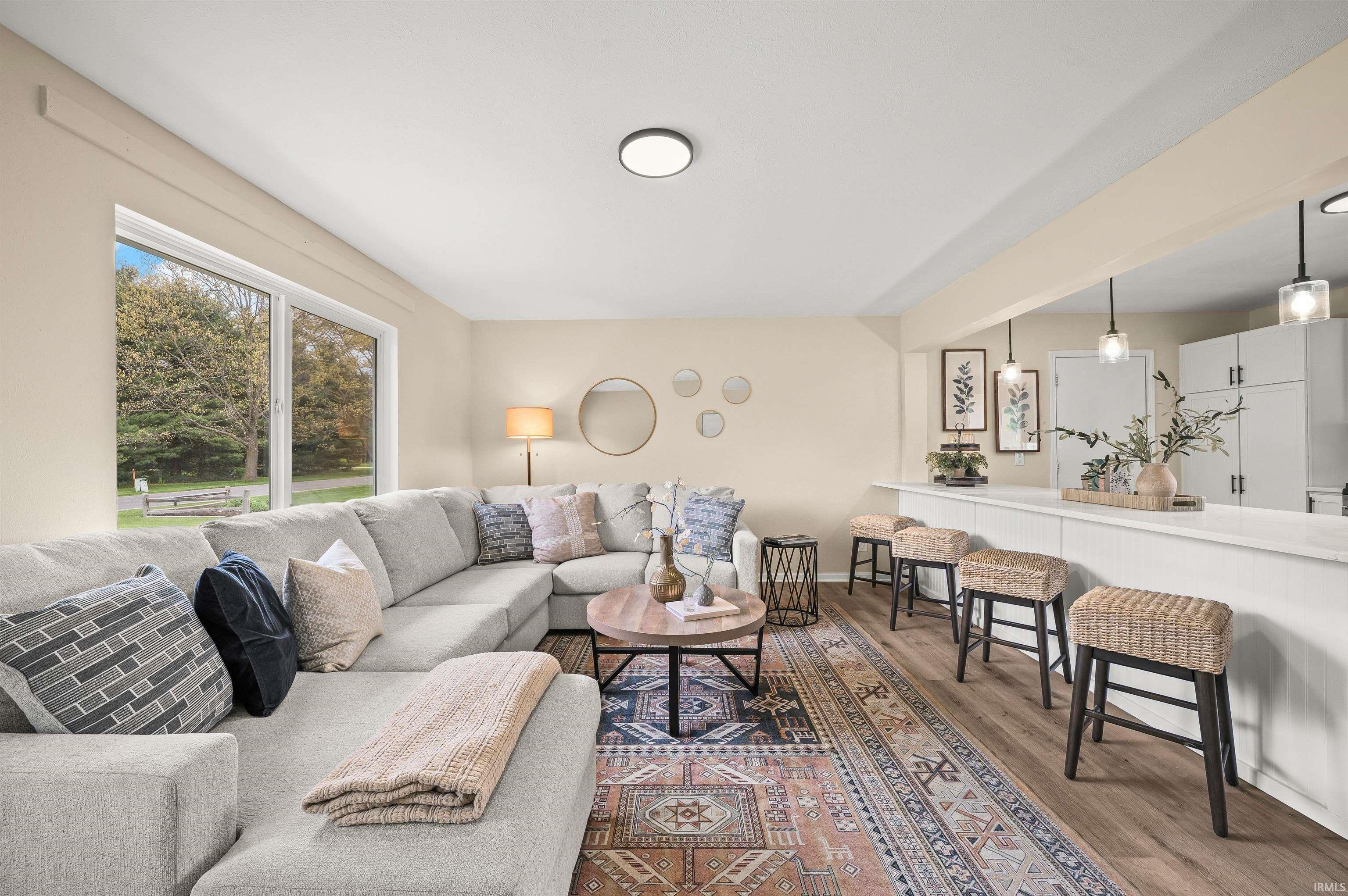 Spacious living area featuring large windows, wood-finish flooring, a breakfast bar with built-in cabinetry, and pendant lighting