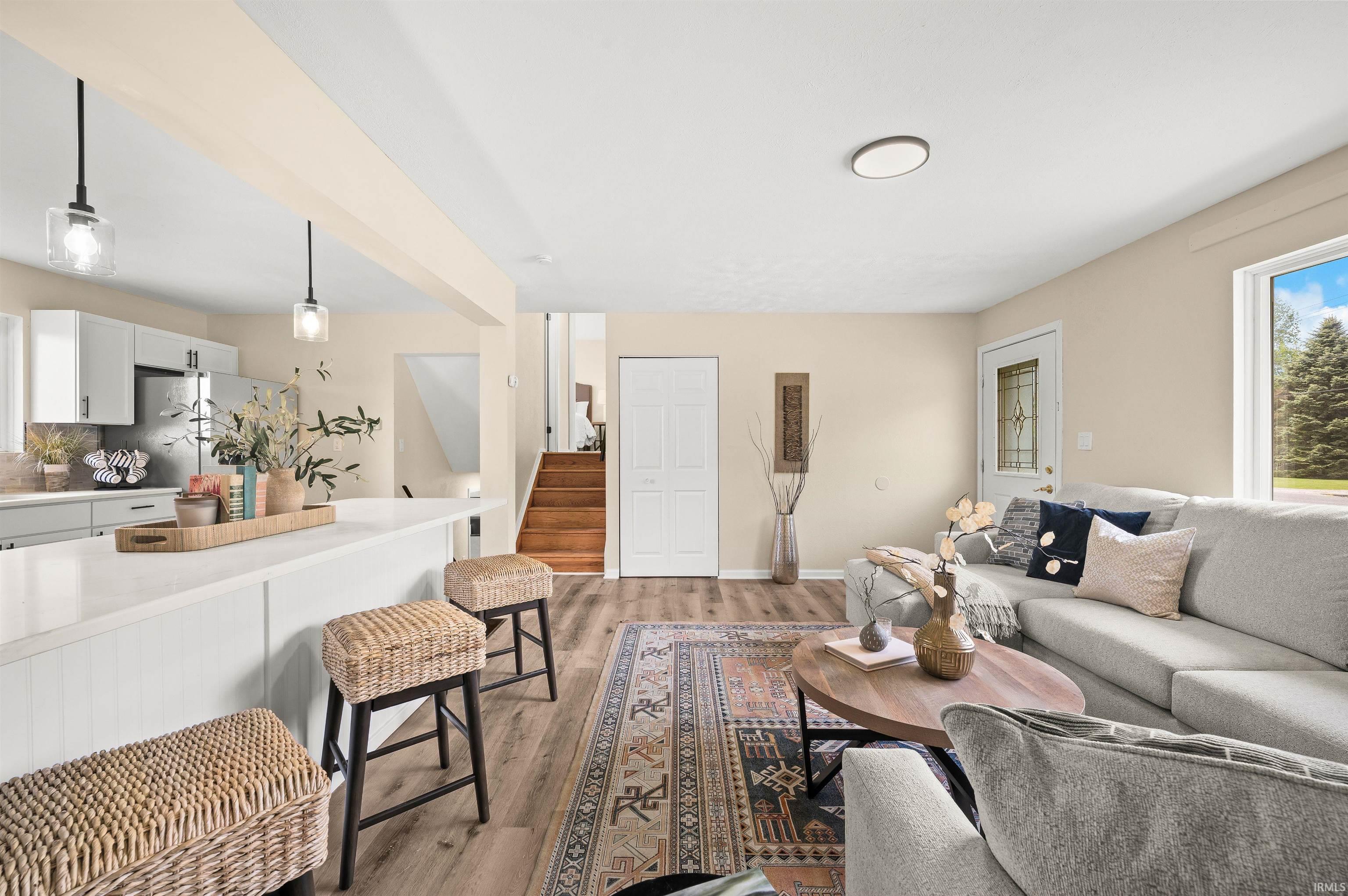 Open-concept living space featuring wood-finish flooring, a white kitchen island with an extended countertop, and sleek pendant lighting