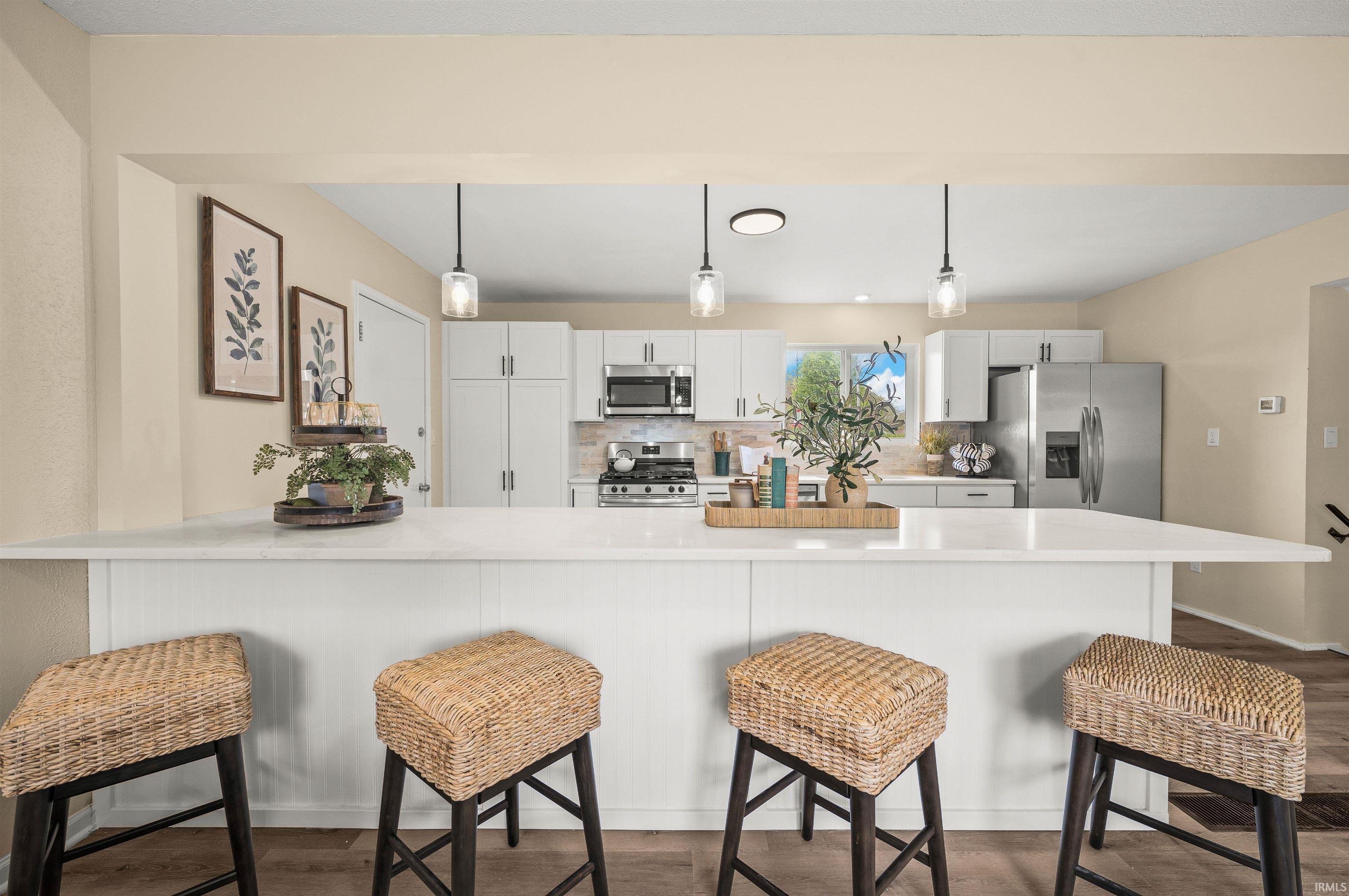 Open-concept kitchen featuring an expansive island with white countertop, white cabinetry, stainless steel appliances, and pendant lighting
