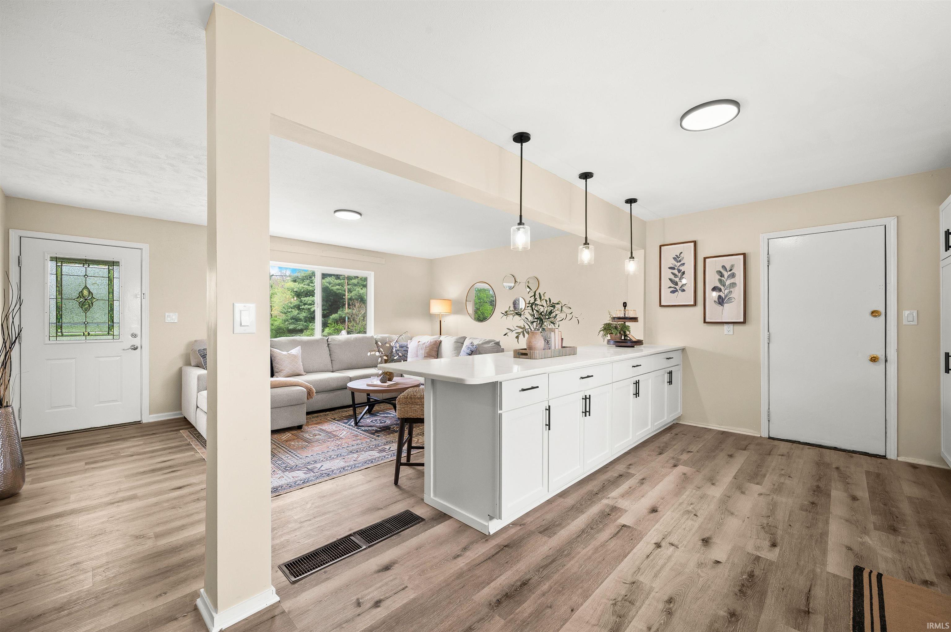 Open-concept interior featuring wood-finish flooring, white cabinetry with black hardware, recessed lighting, and a front entry door with leaded glass accents