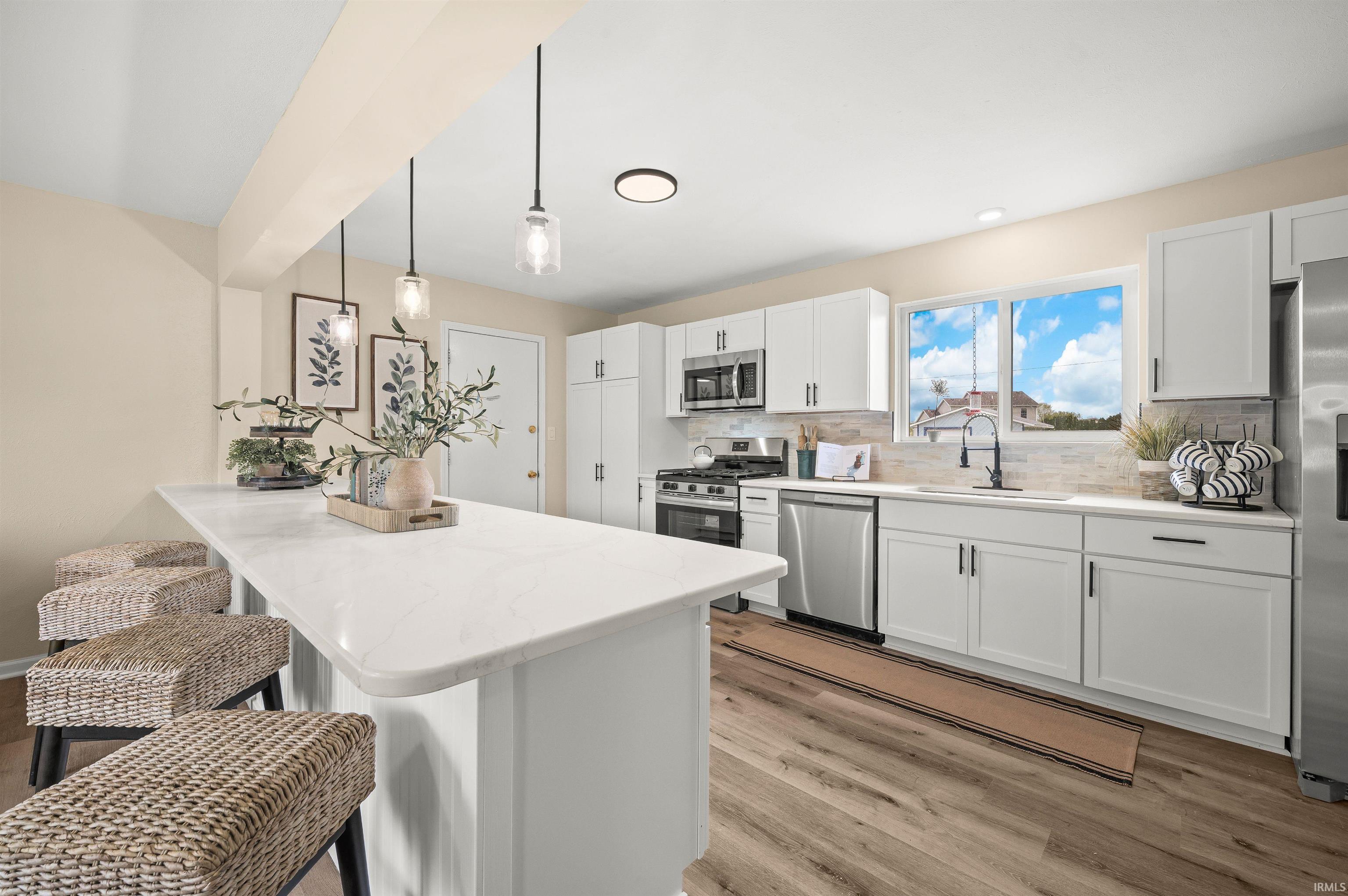 Contemporary kitchen featuring a breakfast bar with pendant lighting, white shaker-style cabinetry, stainless steel appliances, a tile backsplash, and wood-finish flooring
