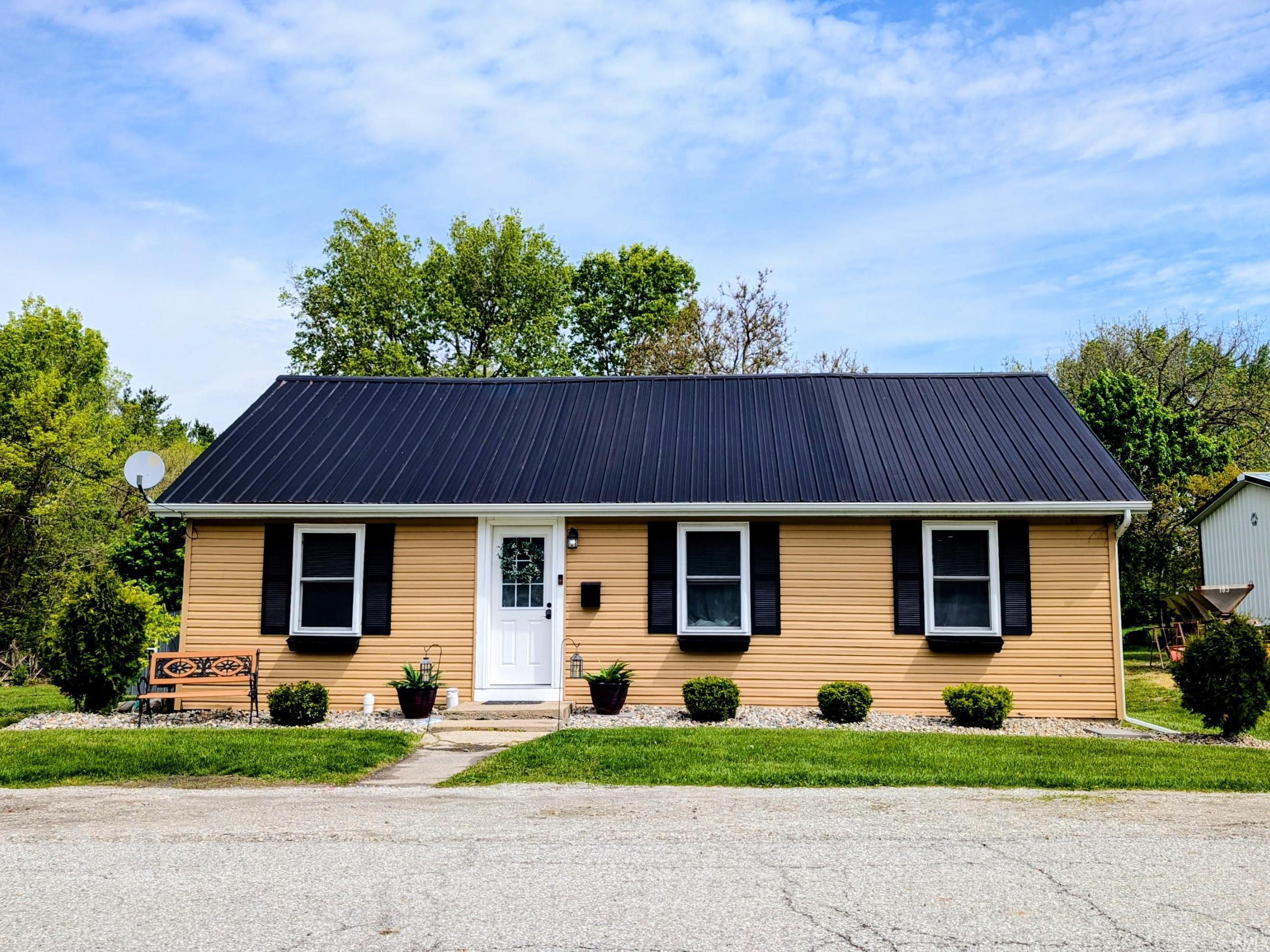 Exterior features include horizontal siding, a dark metal roof, and a white front door