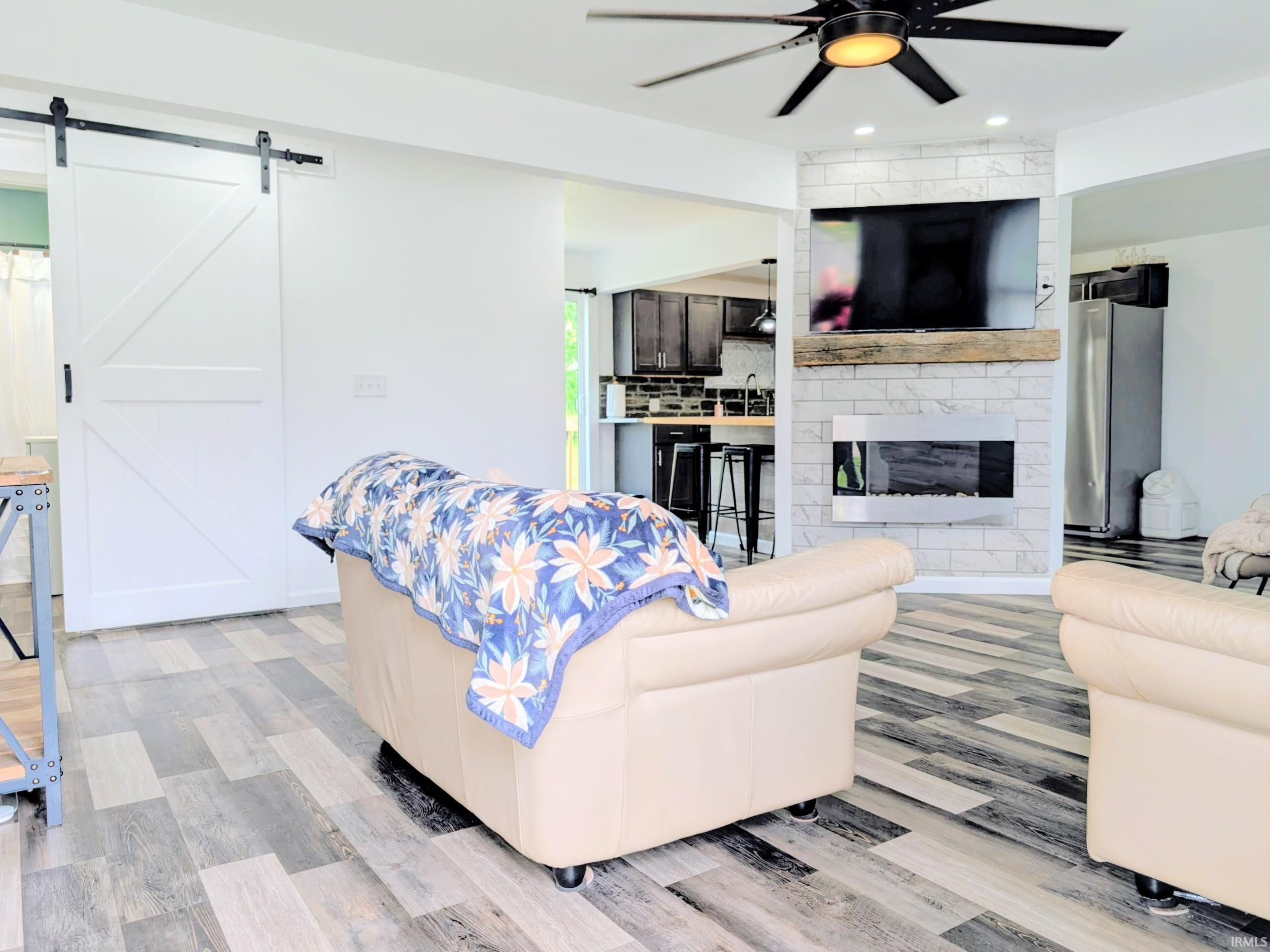 Living area featuring wood-finish flooring, a contemporary ceiling fan, and a fireplace with a white brick surround and wood mantel