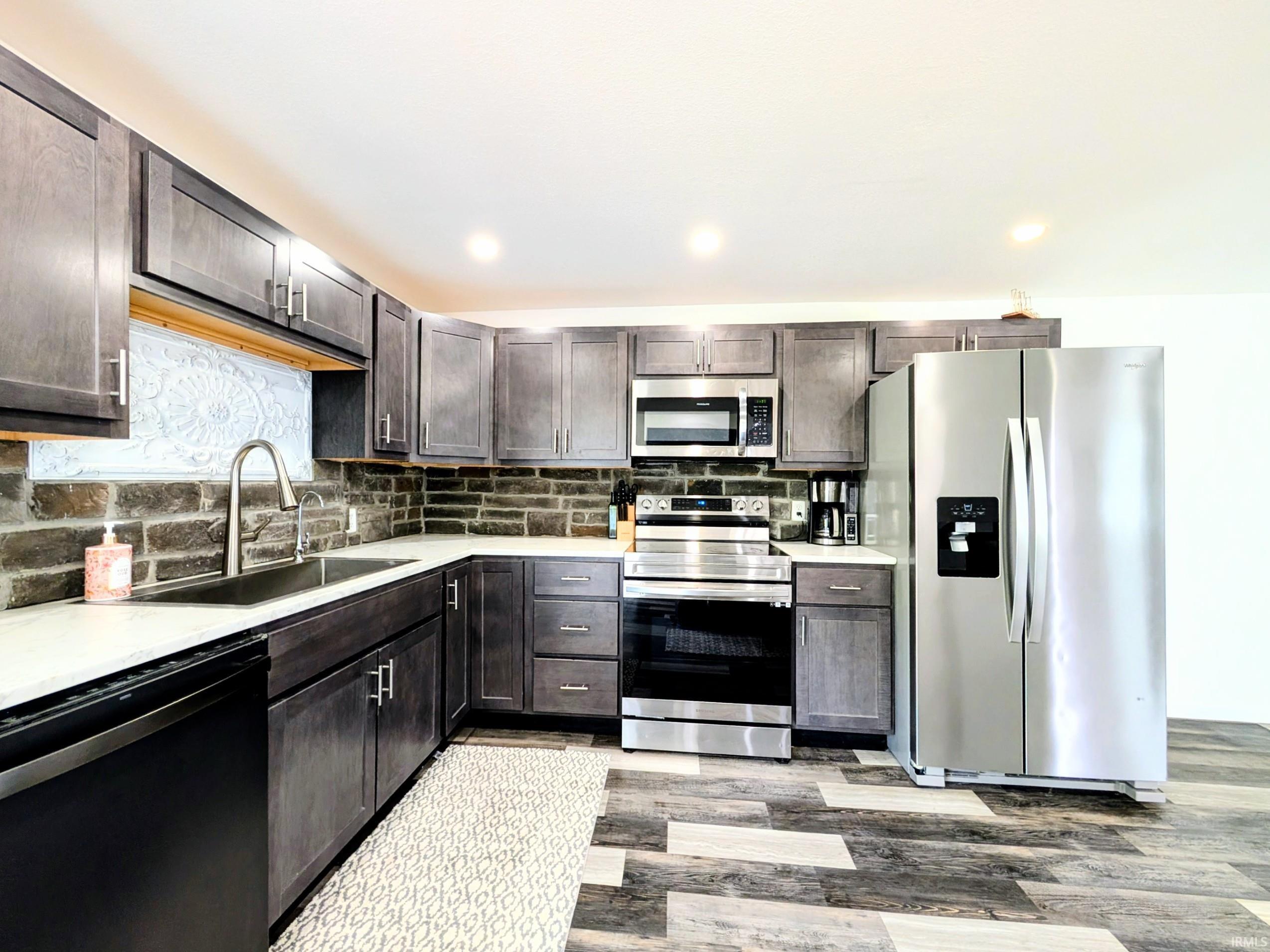 Kitchen featuring gray cabinetry, white countertops, a dark brick-style backsplash, stainless steel appliances, and multi-toned wood-finish flooring