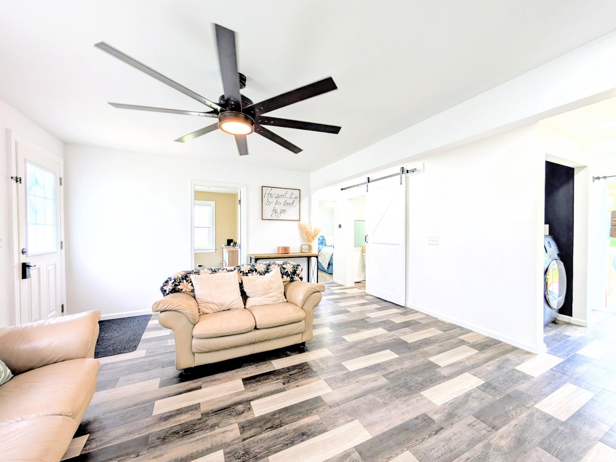 Interior space featuring patterned wood-finish flooring, white walls, and a large ceiling fan with integrated lighting