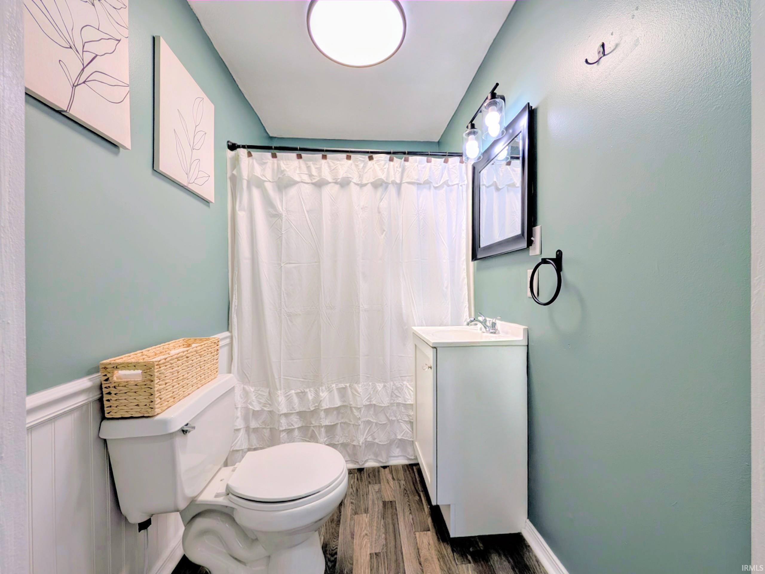 Full bathroom featuring a white vanity with integrated sink, wood-finish flooring, a toilet, and wainscoting