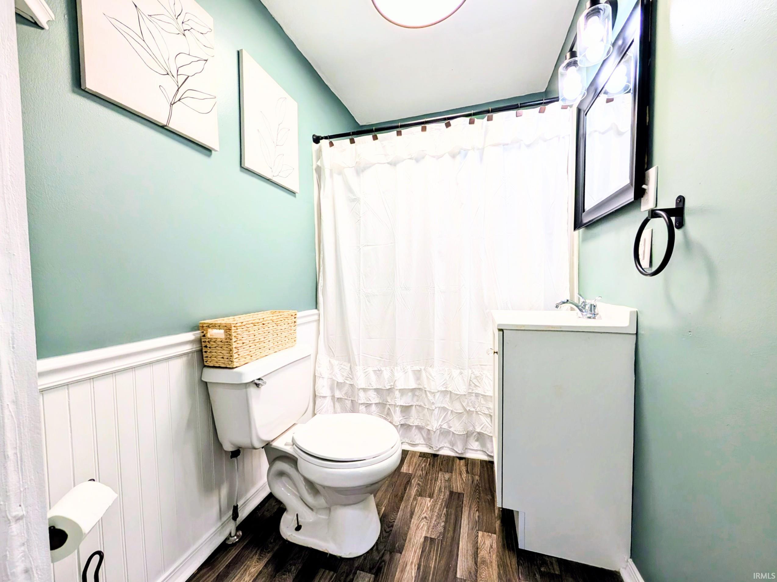 Bathroom featuring wood-finish flooring, white beadboard wainscoting, and a white vanity with an integrated sink