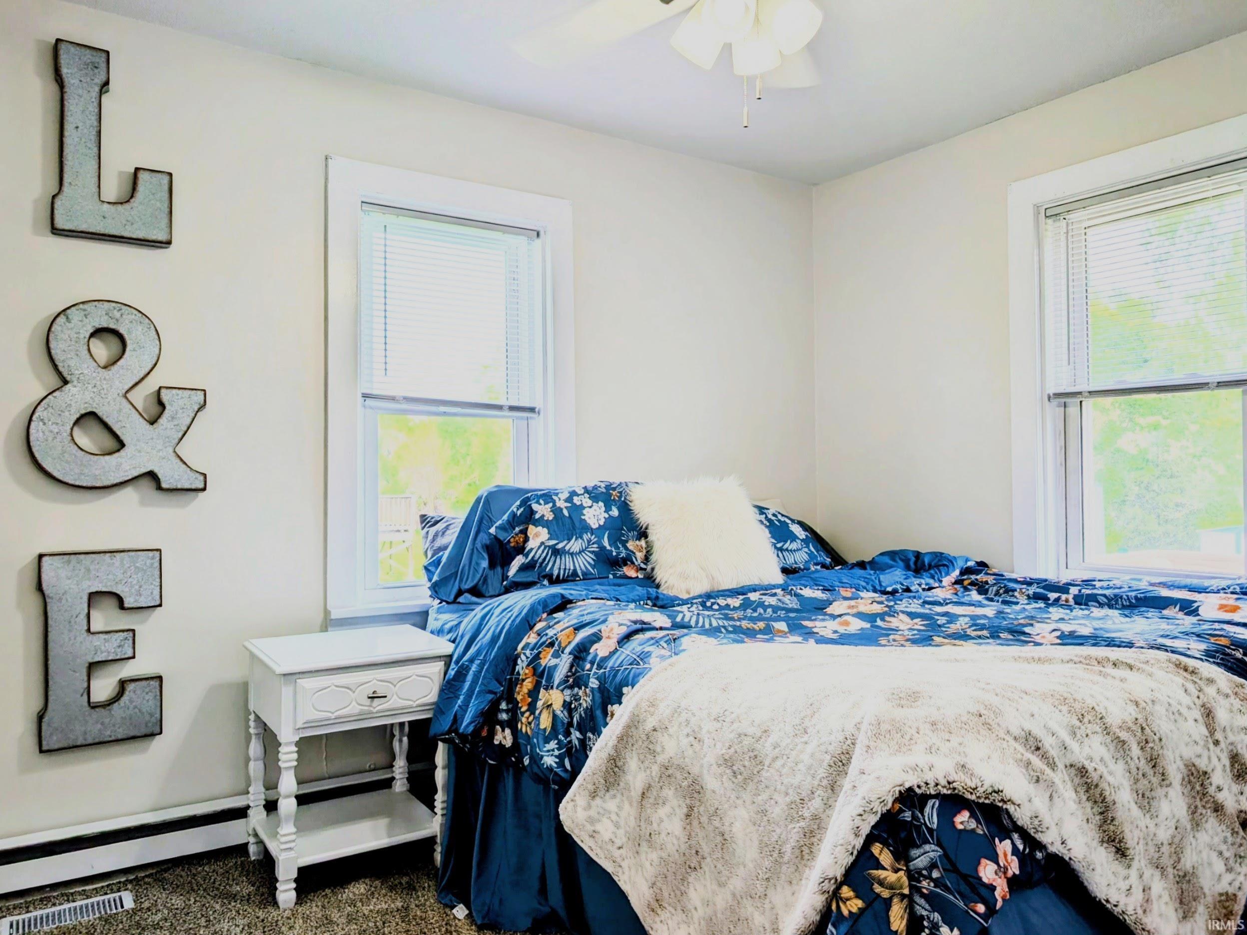 Bright interior room with two windows, carpeted flooring, and a ceiling fan