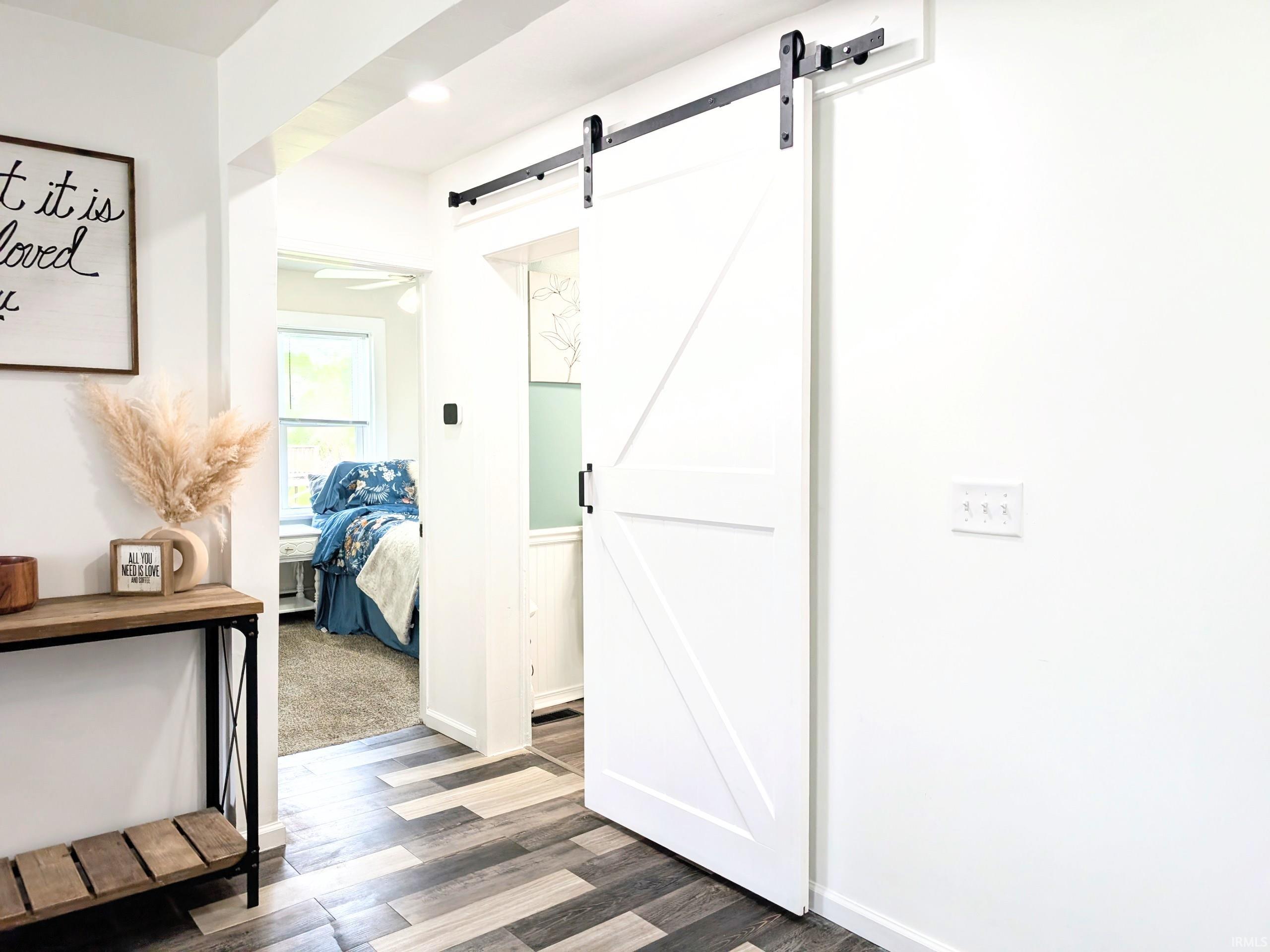 Contemporary white barn door with black hardware, plank-style flooring, white walls, and recessed lighting