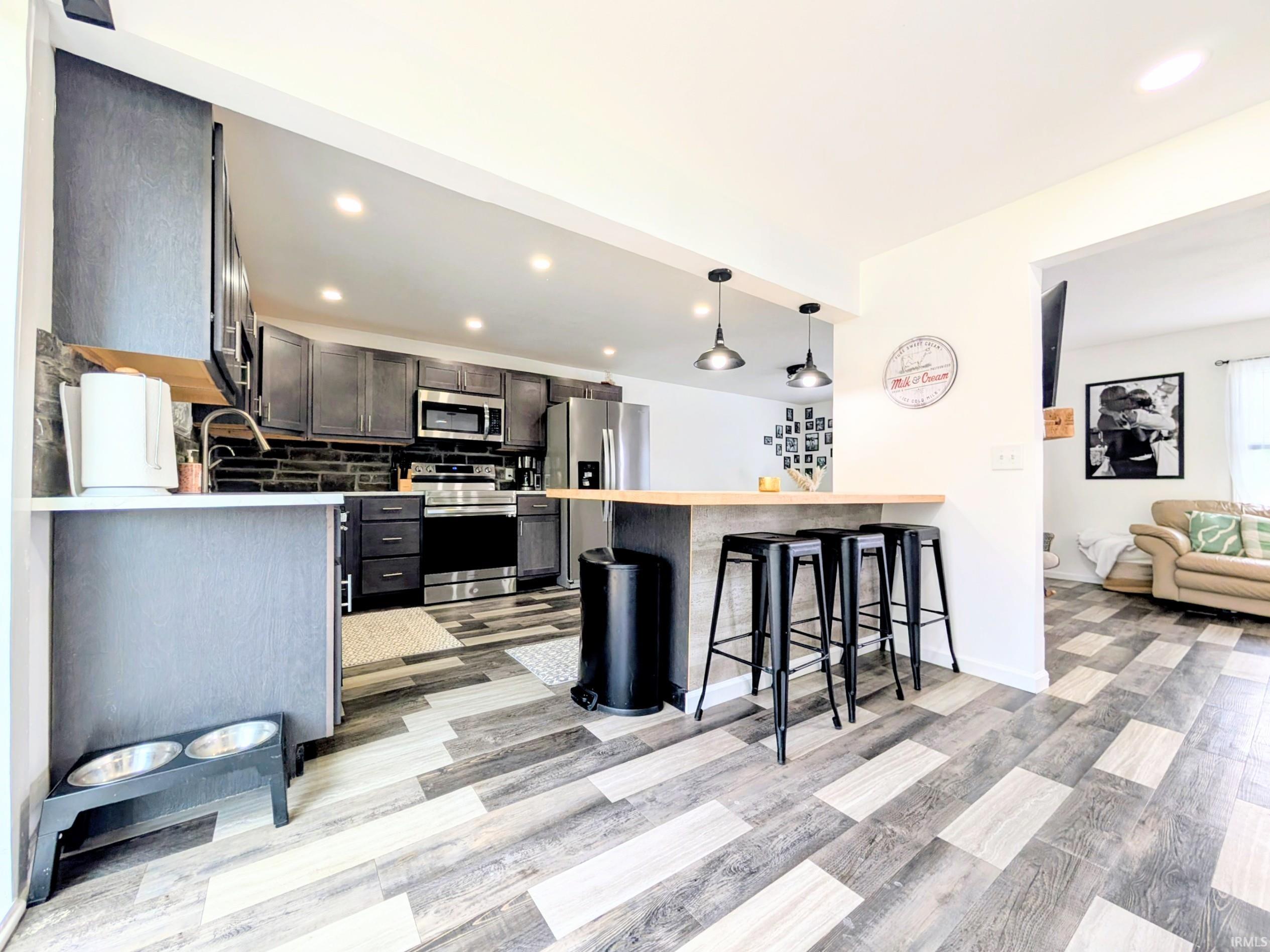Kitchen featuring dark wood-finish cabinetry, stainless steel appliances, a black subway tile backsplash, recessed lighting, and wood-look plank flooring