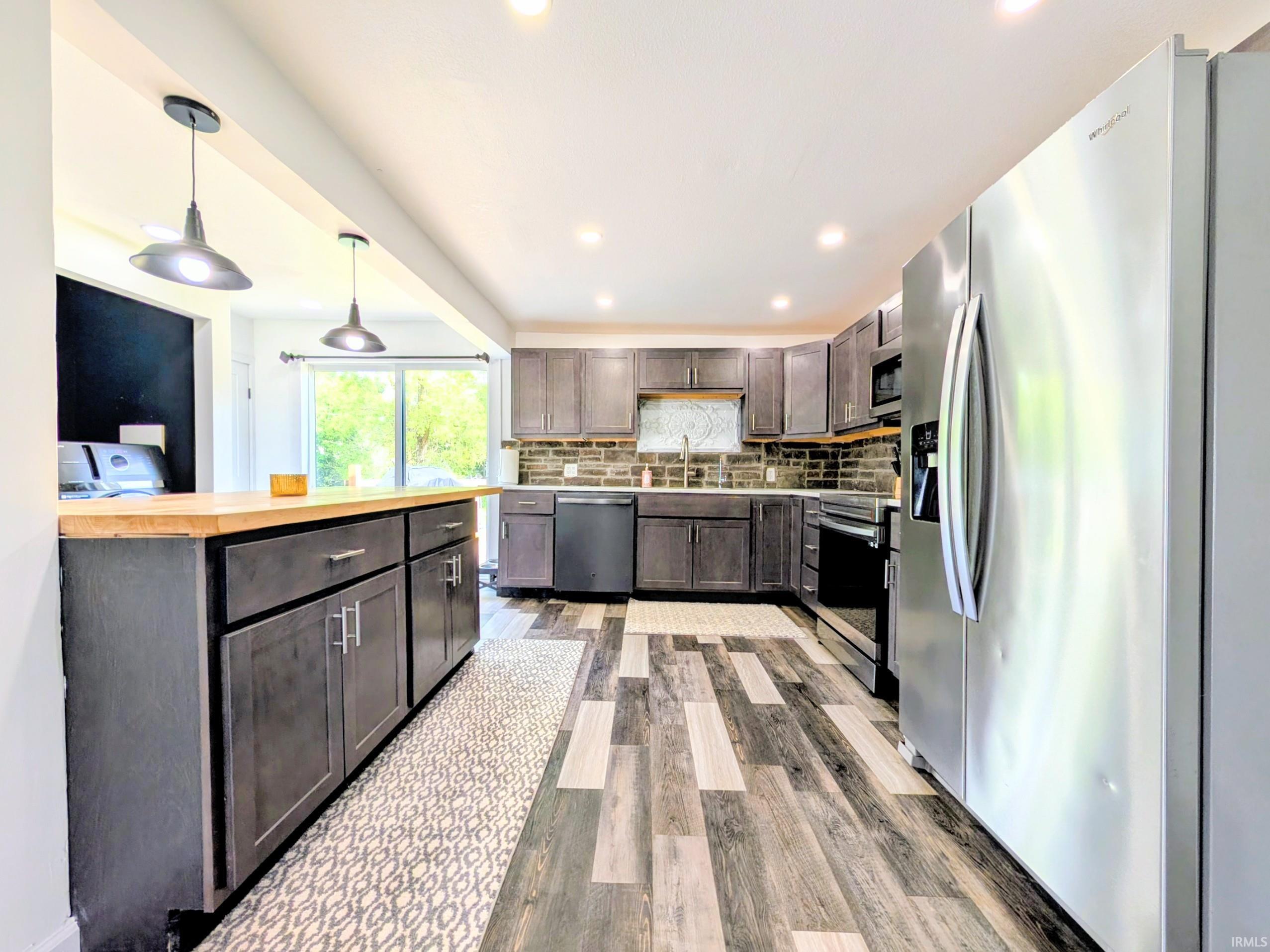 Contemporary kitchen featuring dark wood-finish cabinetry, an extended wood-finish countertop, and stainless-steel appliances